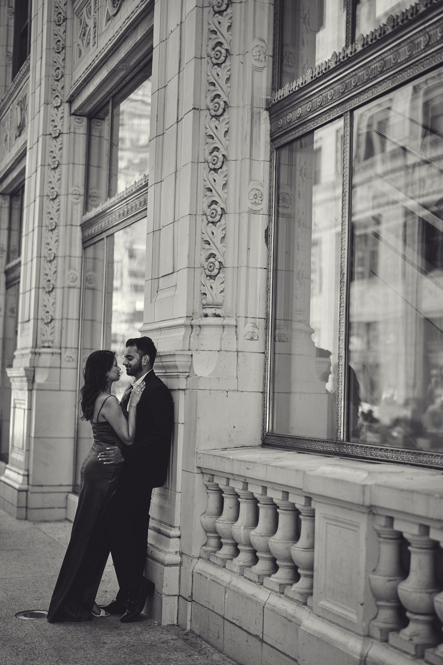 A romantic black and white photograph of a couple embracing by an ornate architectural facade with decorative columns.