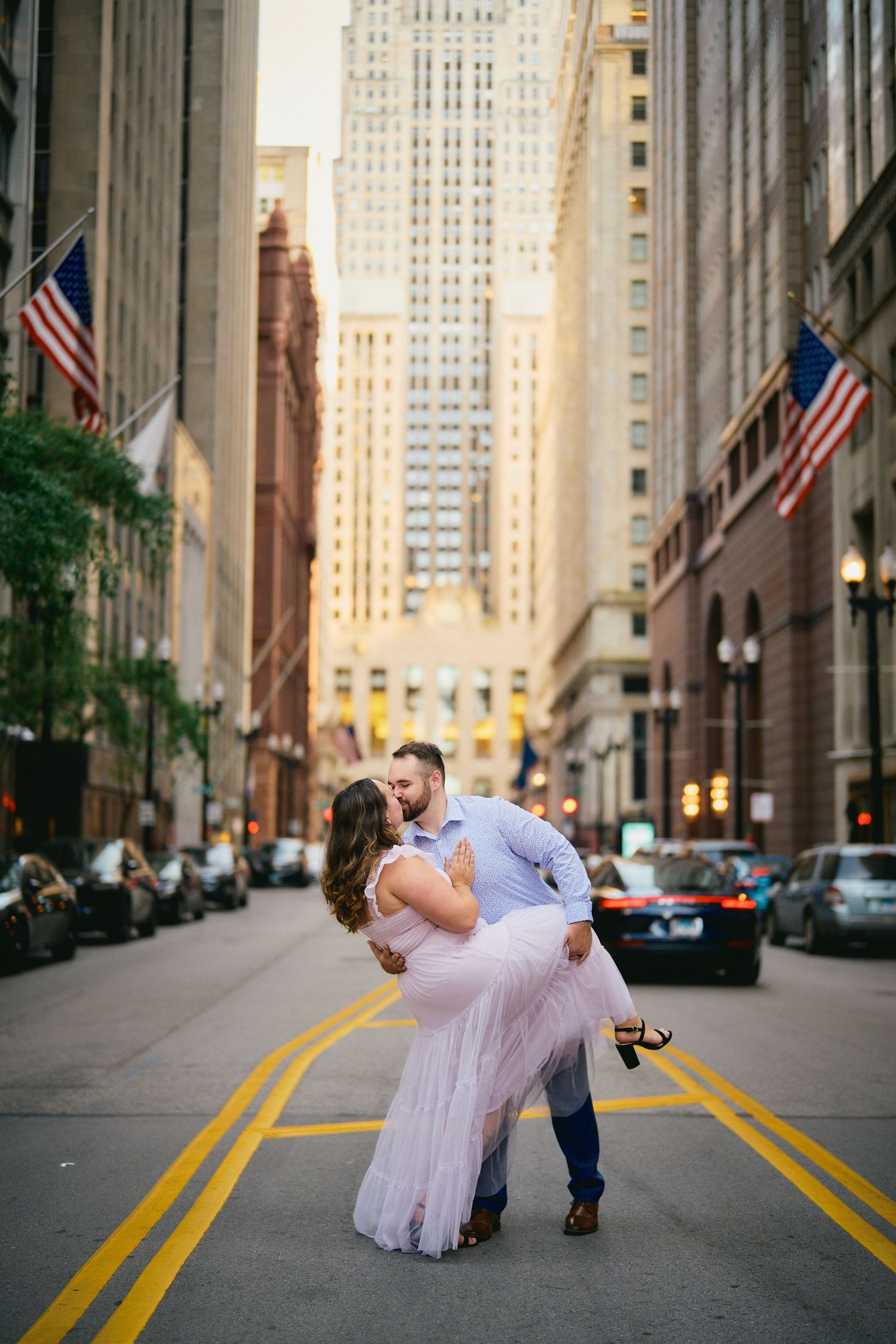 Romantic couple in formal attire dance in the middle of a Chicago street lined with American flags and tall buildings.