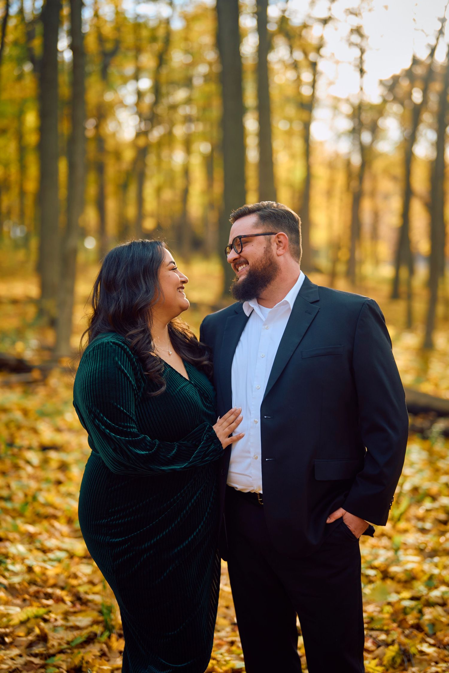 A couple shares a joyful moment together in a fall forest surrounded by golden leaves.