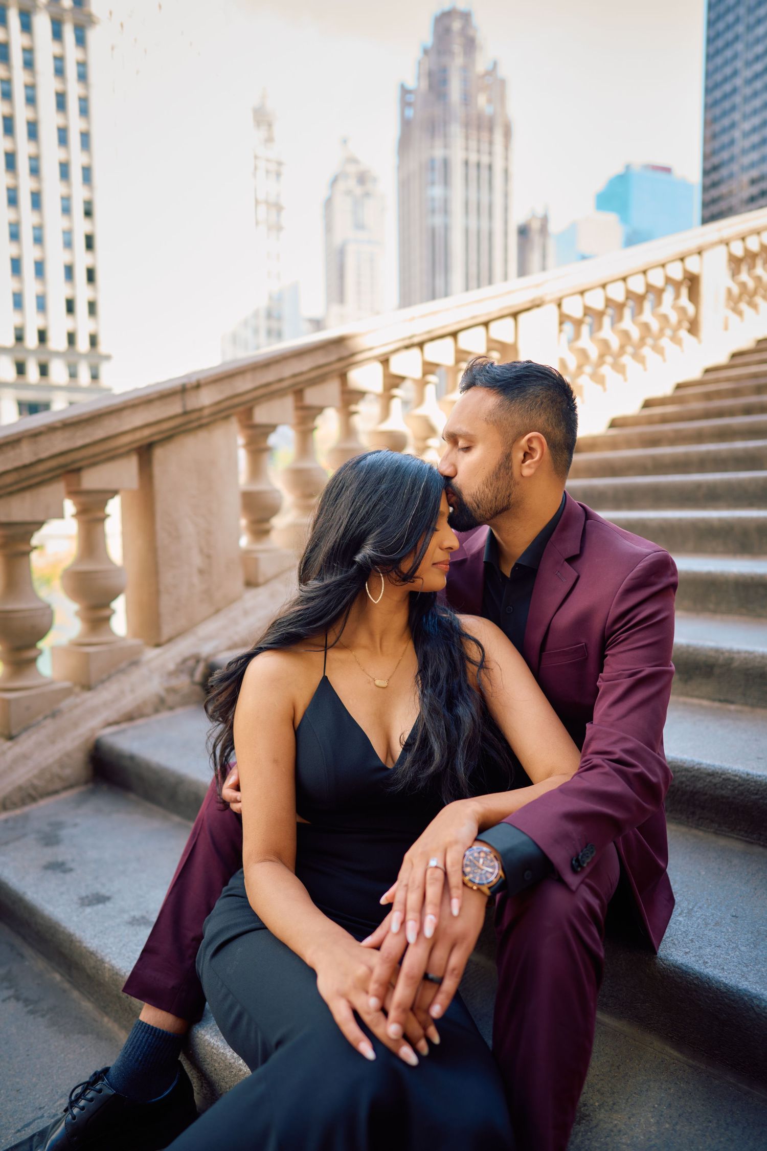 A romantic couple sits together on elegant stone steps in downtown Chicago with skyscrapers in the background.