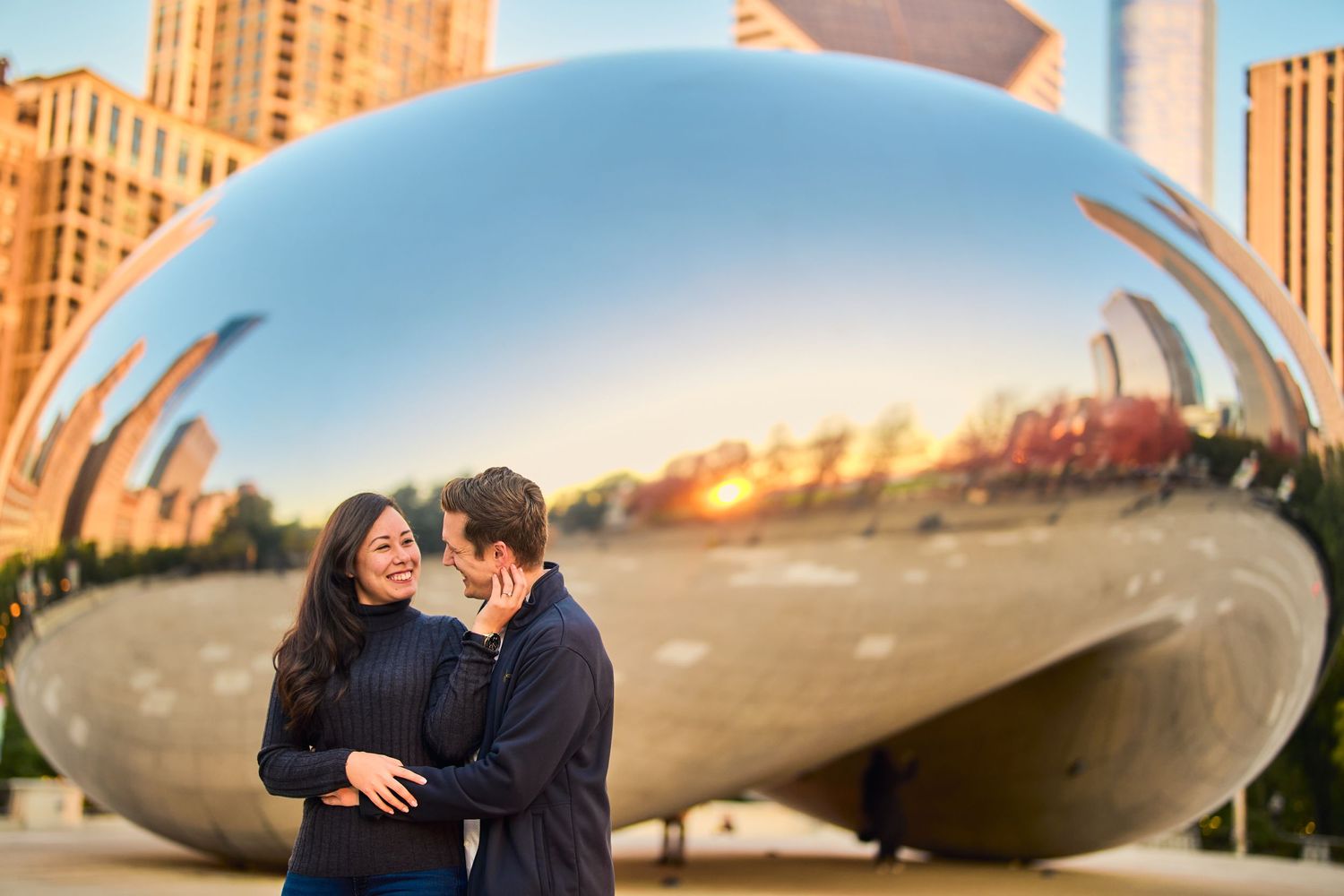 Couple sharing intimate moment in front of Chicago's Cloud Gate sculpture at sunset.