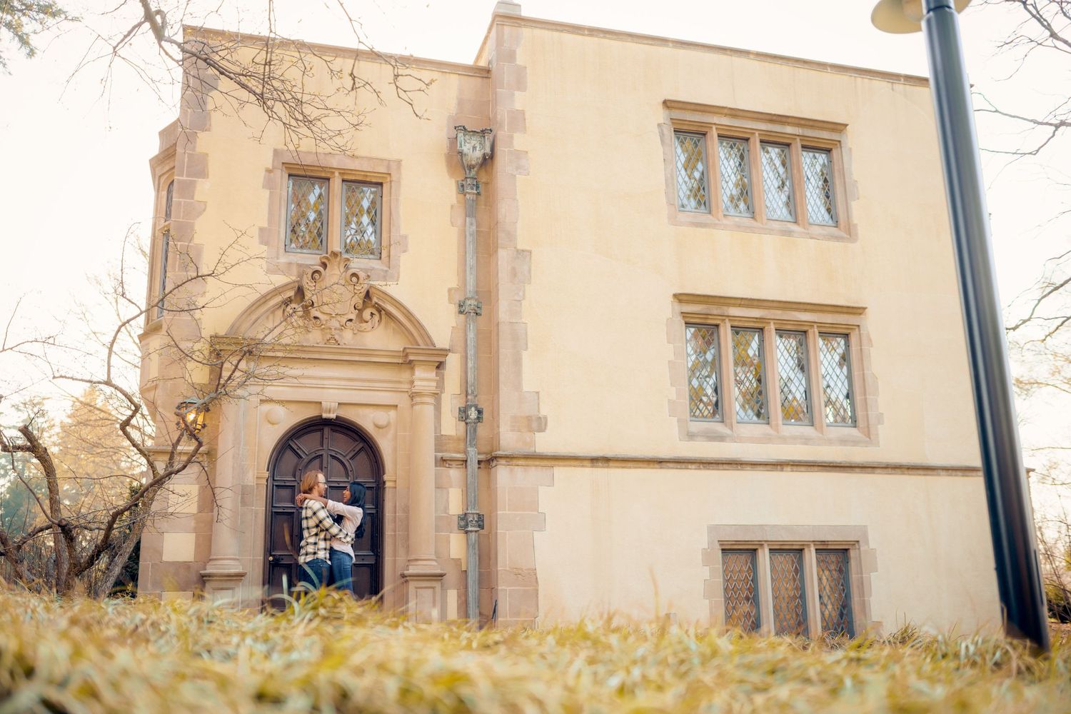 A beige stone building with decorative arched entrance and windows photographed from a low angle amid autumn grass.