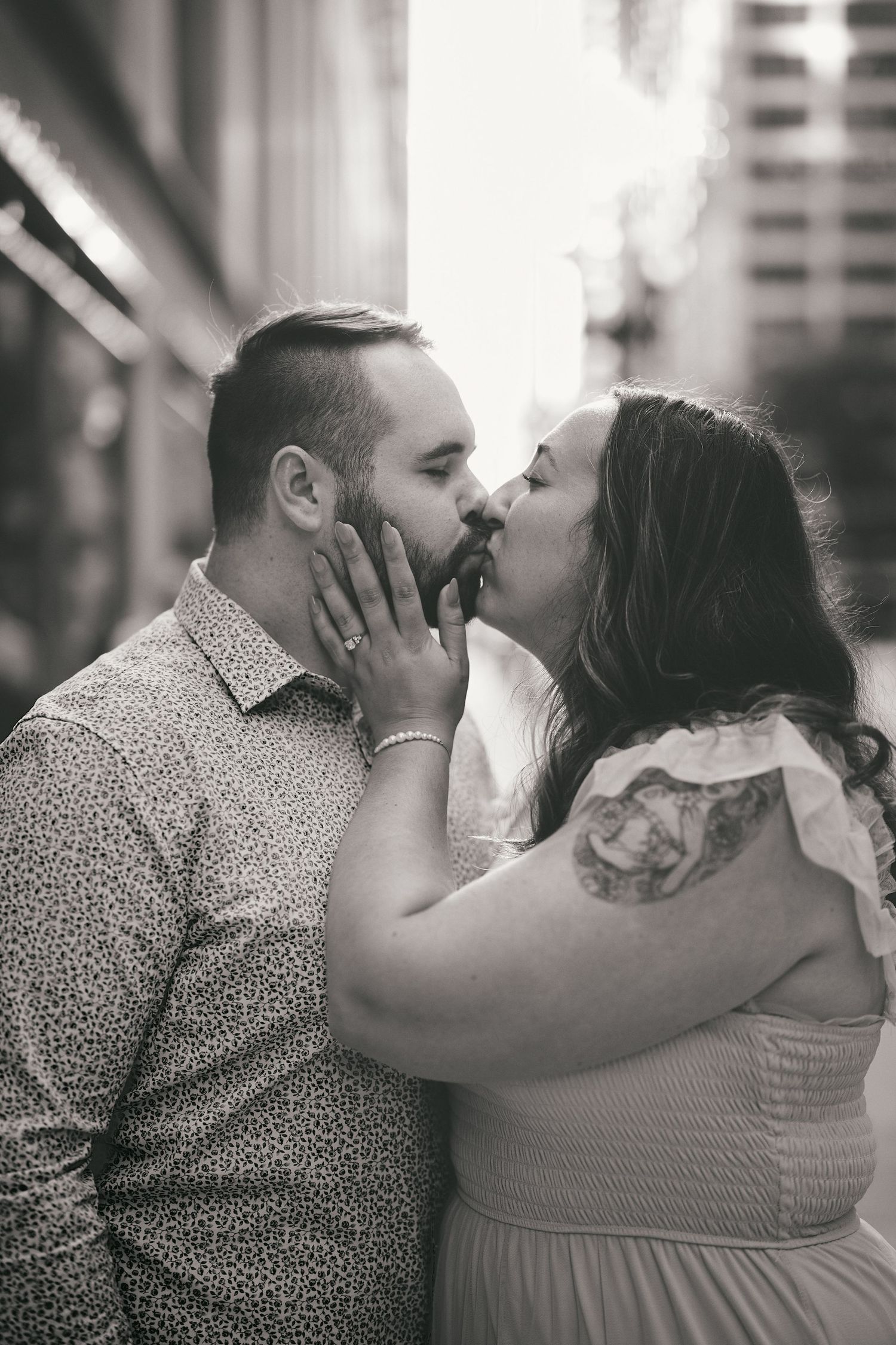 A romantic black and white portrait of a couple sharing a tender kiss on an urban street.