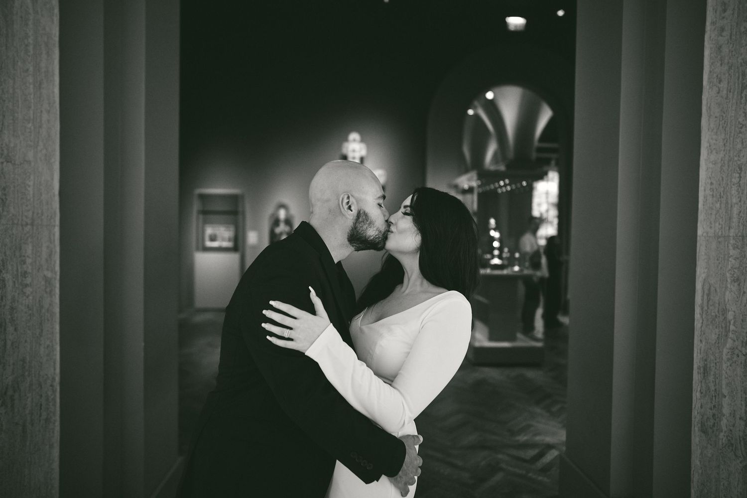 A couple shares an intimate dance moment in a dimly lit hallway with elegant architecture and ambient lighting.