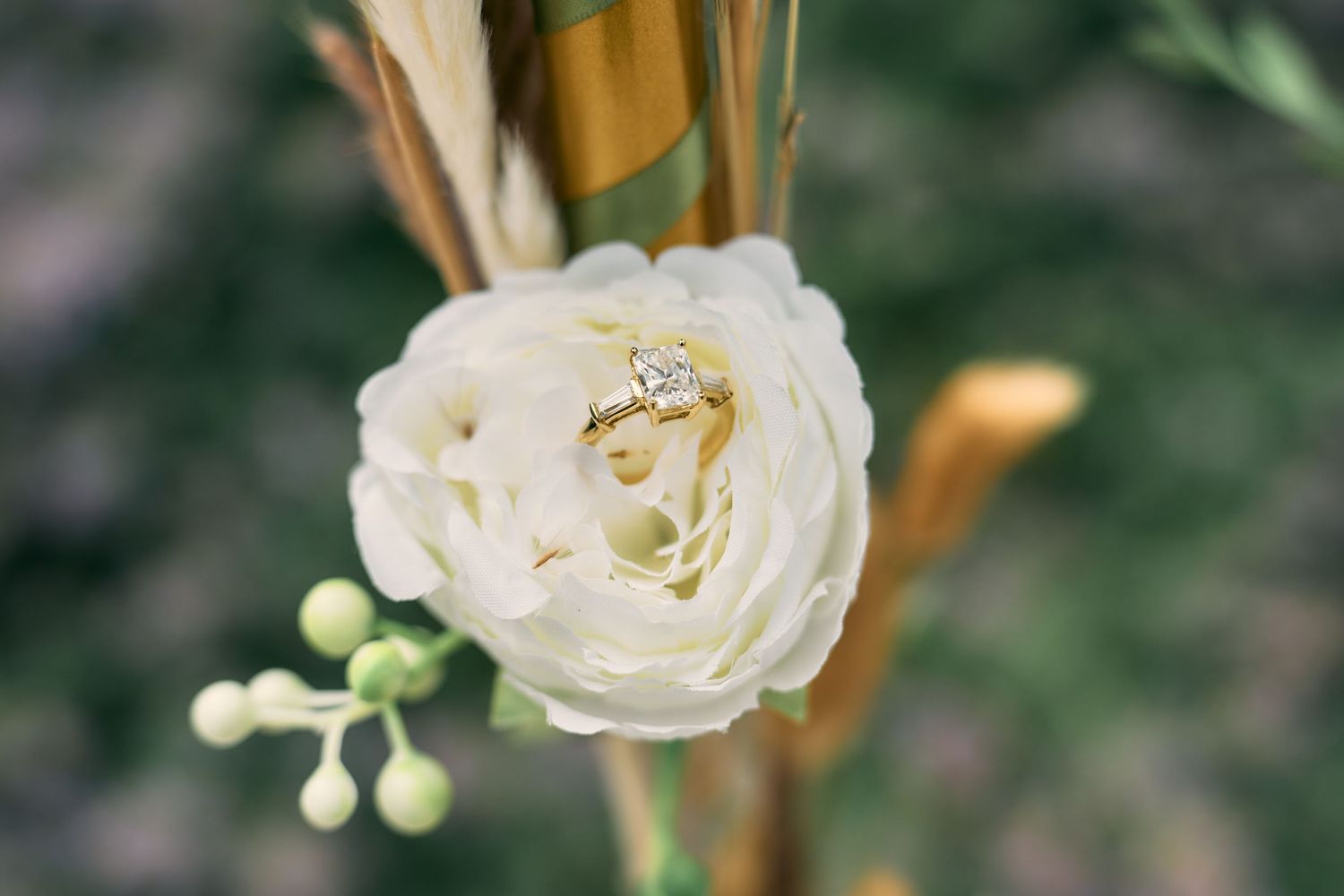 Wedding rings nestled inside a delicate white rose bloom with soft green foliage in the background.