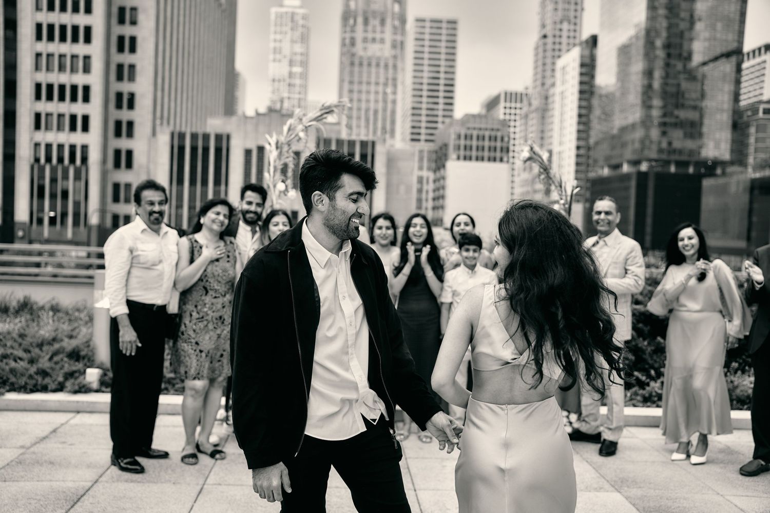 A couple dances joyfully in a Chicago rooftop garden with the city skyline and other guests in the background.