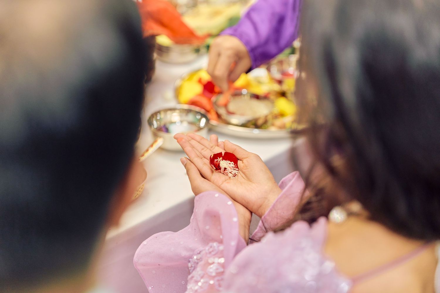 Hand in pink lacy sleeve holds up a small garnish or food item during a dining event.