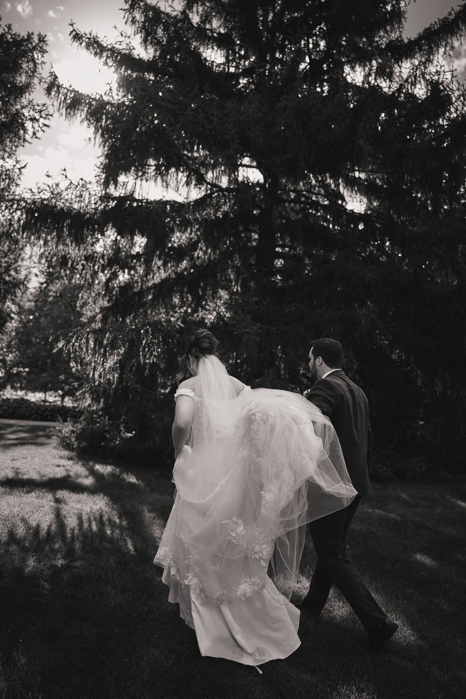 Black and white photos capture a couple dancing outdoors among evergreen trees with the bride's dress flowing in motion.