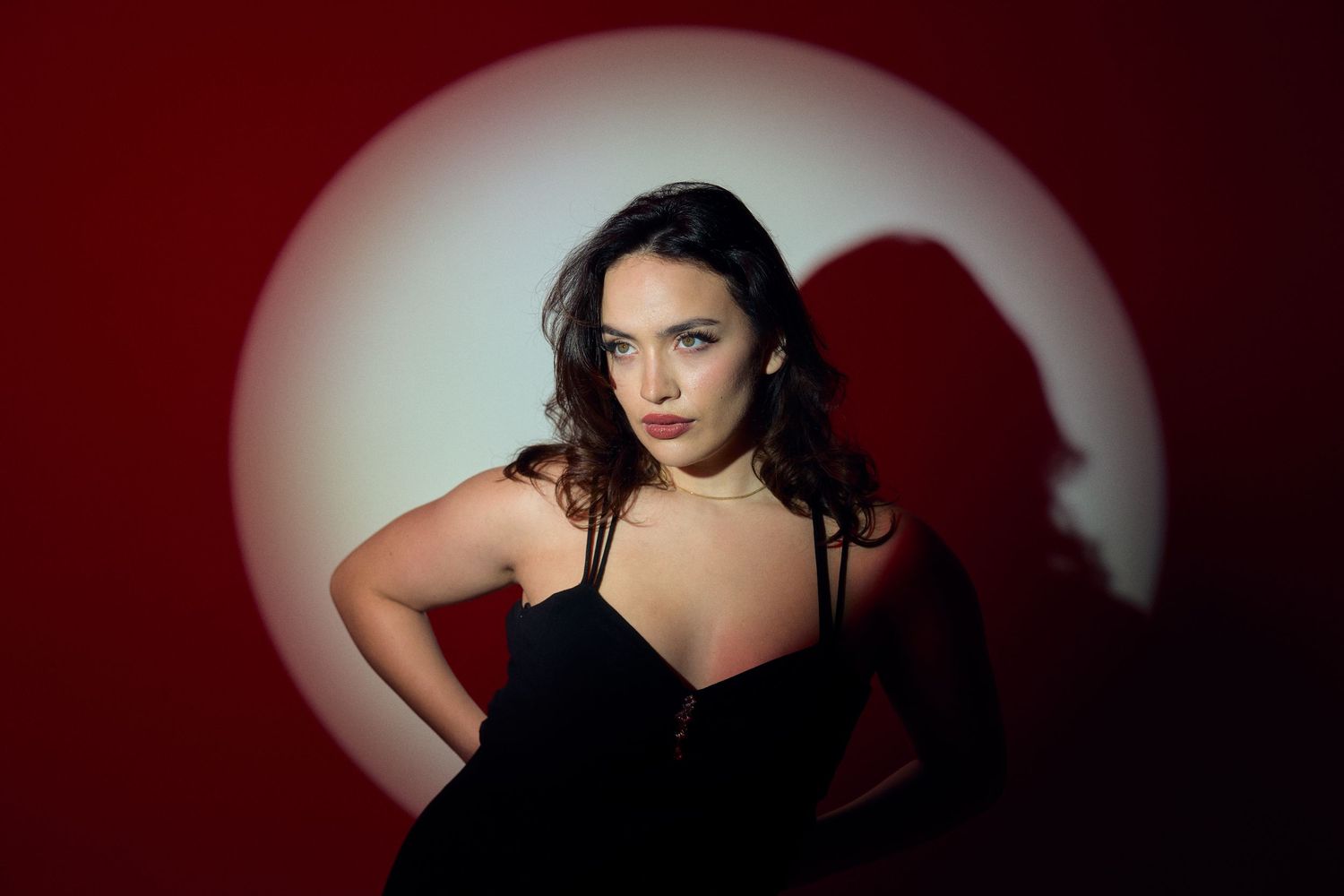 Dramatic portrait of woman in black dress against red background with spotlight effect.