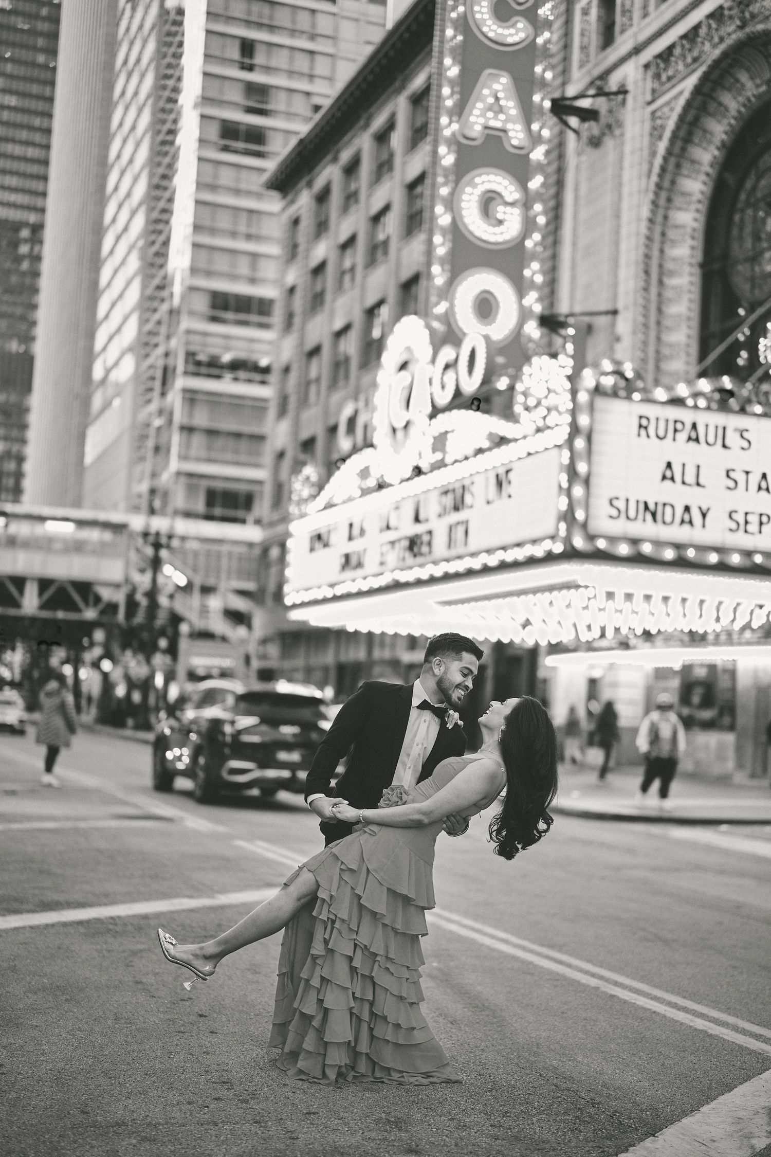 A romantic couple embraces in front of a vintage Chicago Theater marquee in black and white photograph.