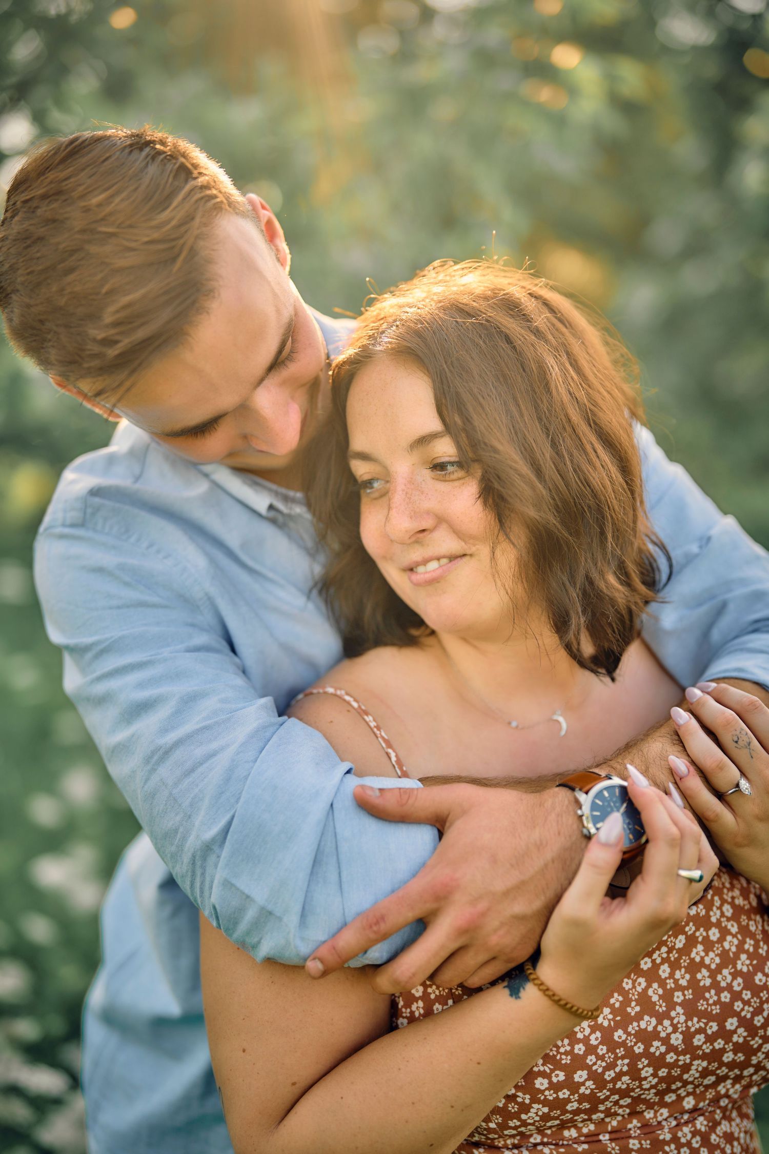 Romantic couple embracing outdoors in warm sunlight with natural bokeh background.