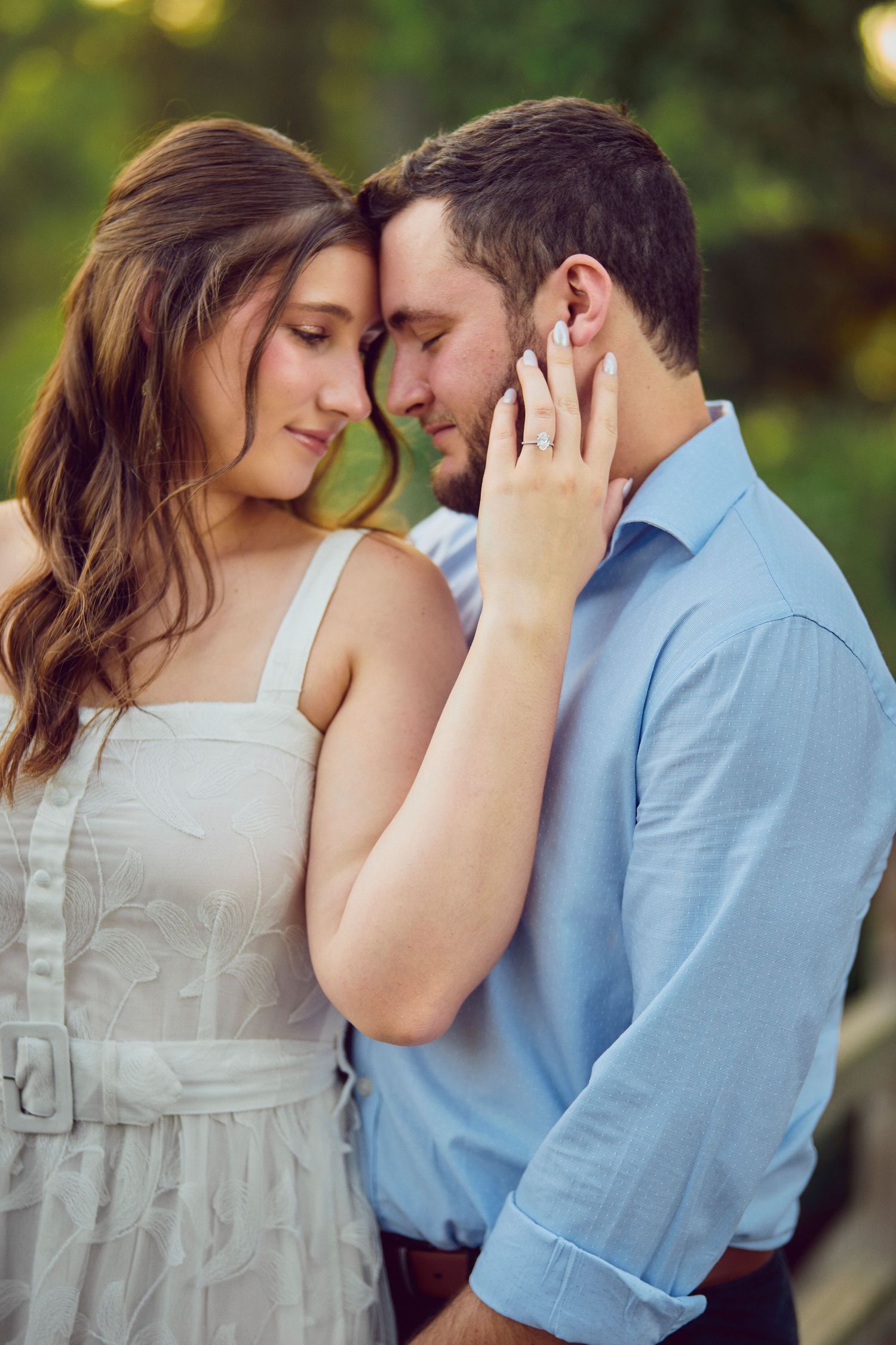 A romantic moment shared between a couple in a white dress and blue shirt standing close together outdoors.