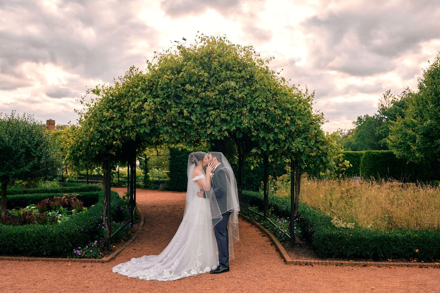 Romantic outdoor wedding ceremony under tall trees with dramatic cloudy skies and natural landscaping.