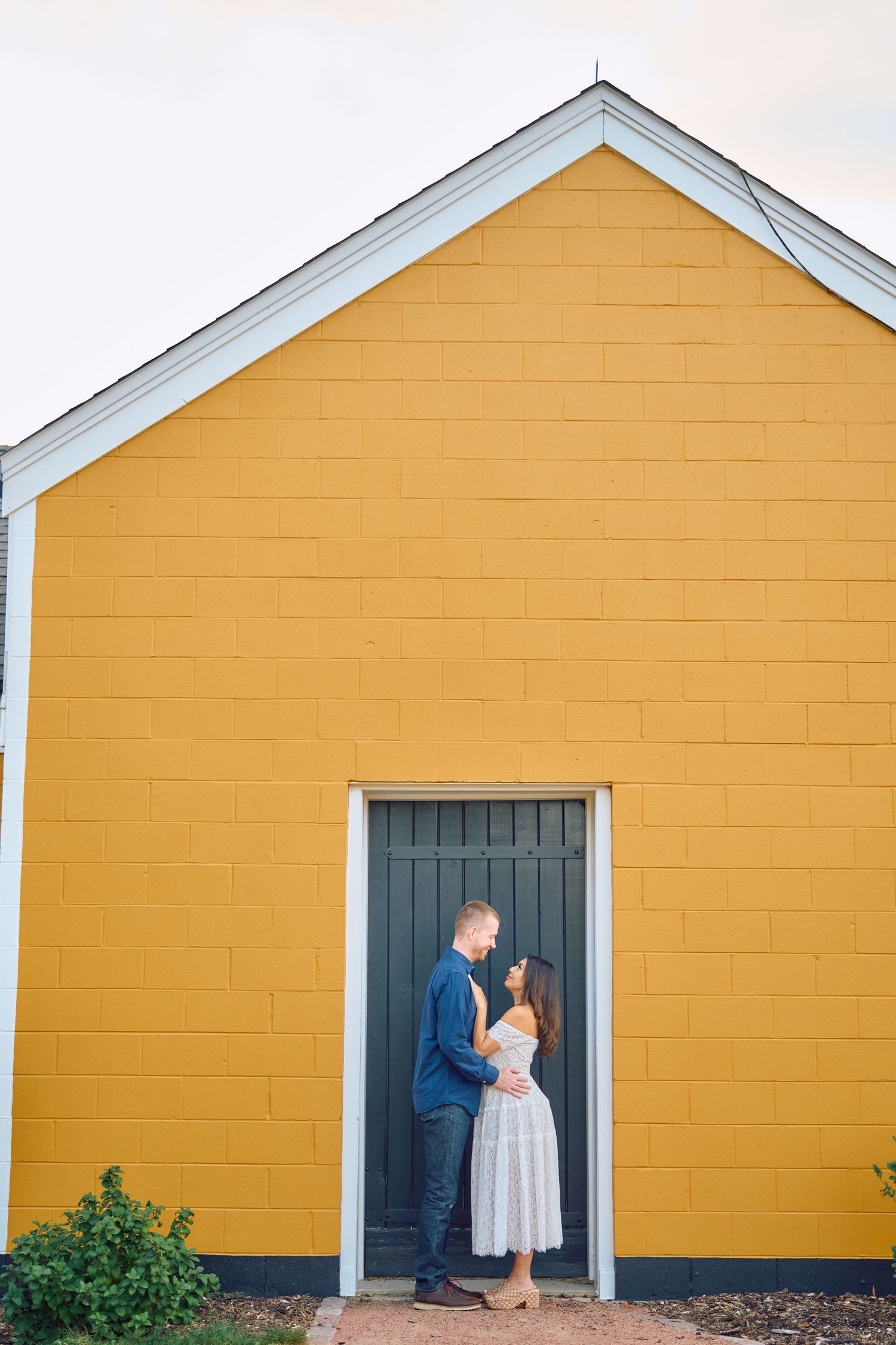 A couple stands in a doorway against a bright yellow building with white trim.