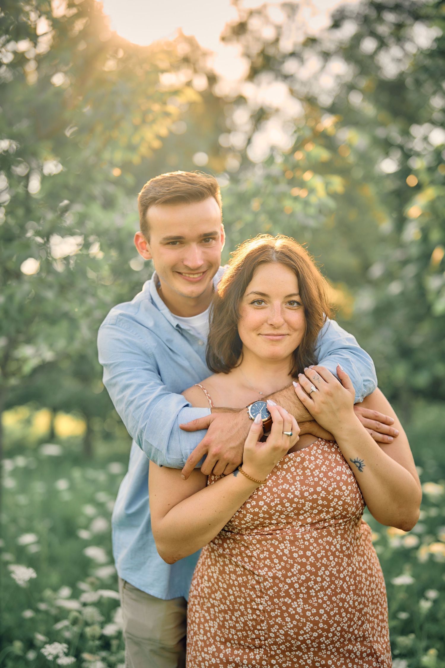 Happy couple embraces outdoors in the afternoon sunlight, surrounded by dreamy bokeh and greenery.