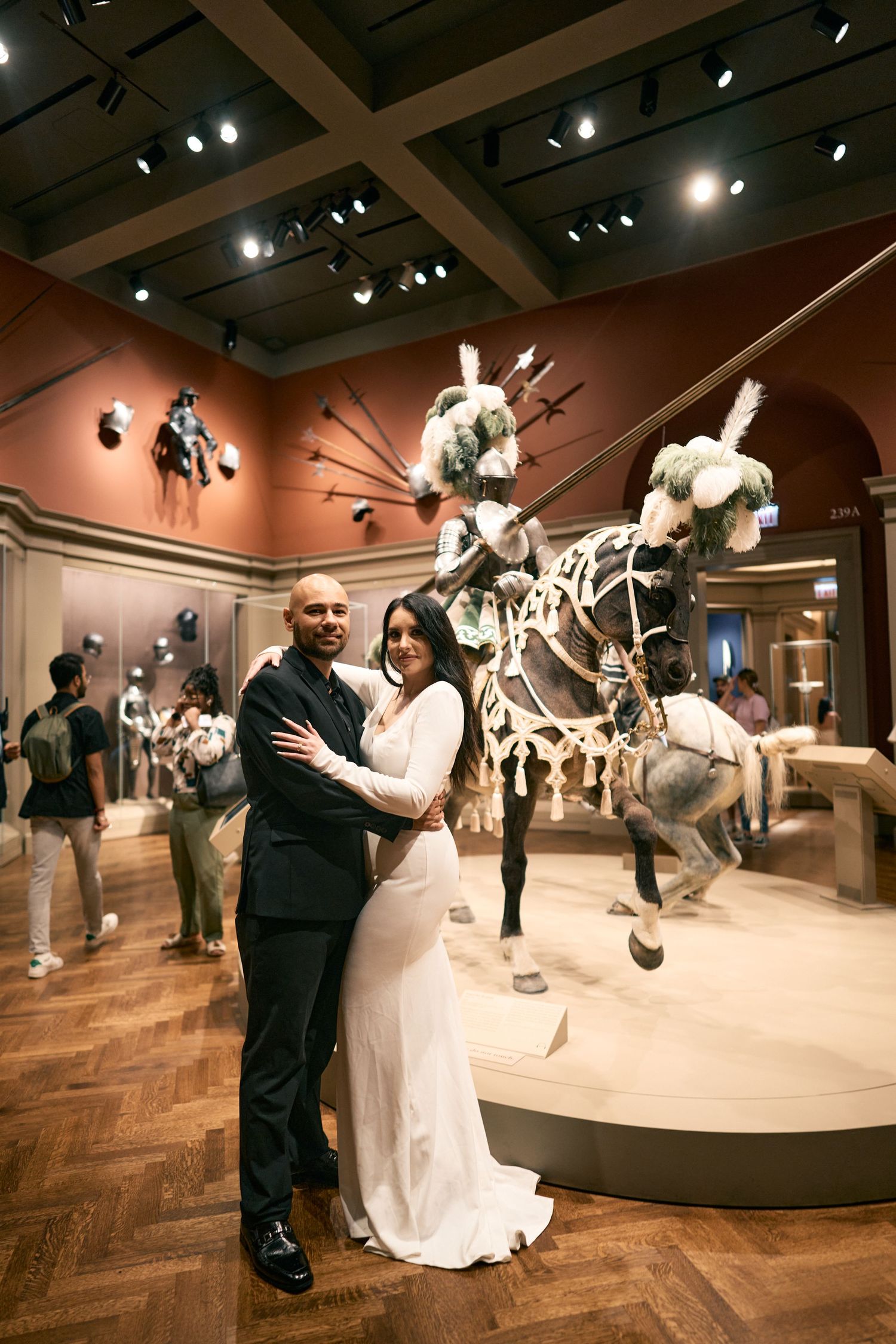 Couple poses in formal attire at a museum exhibit featuring mounted equestrian displays and artifacts.