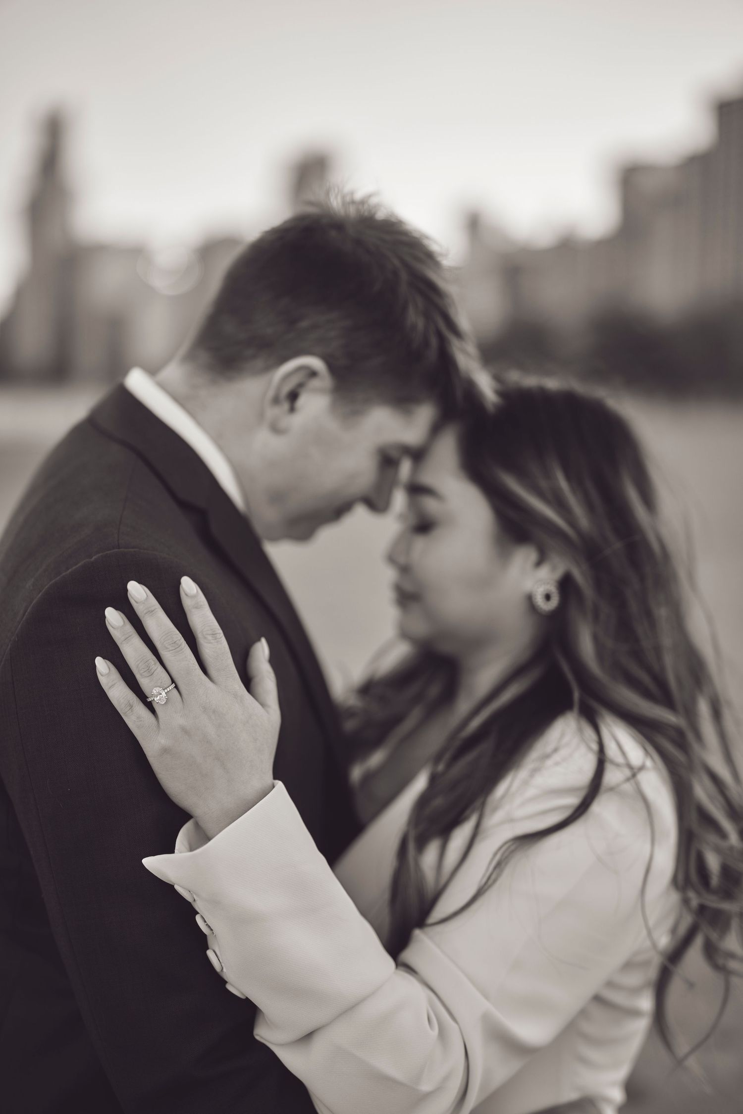 A romantic black and white engagement photo showing a couple in an intimate moment with a sparkling ring on display.