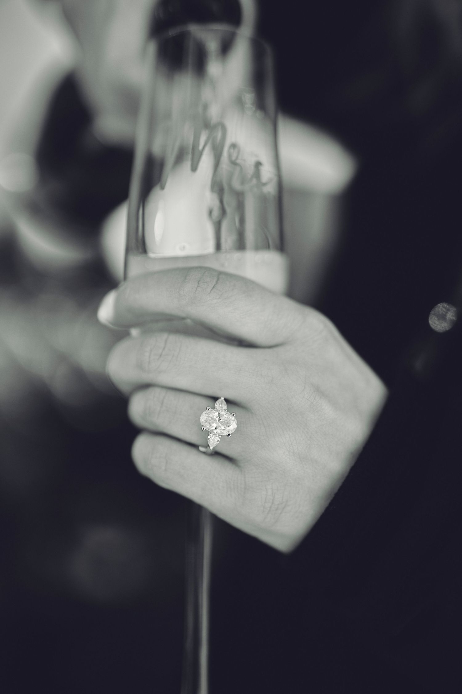 A close up black and white photo of an engagement ring on a hand holding a champagne glass.