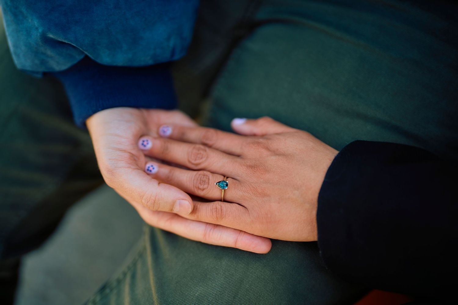 Two hands intertwined showing off an elegant turquoise engagement ring in a closeup shot.