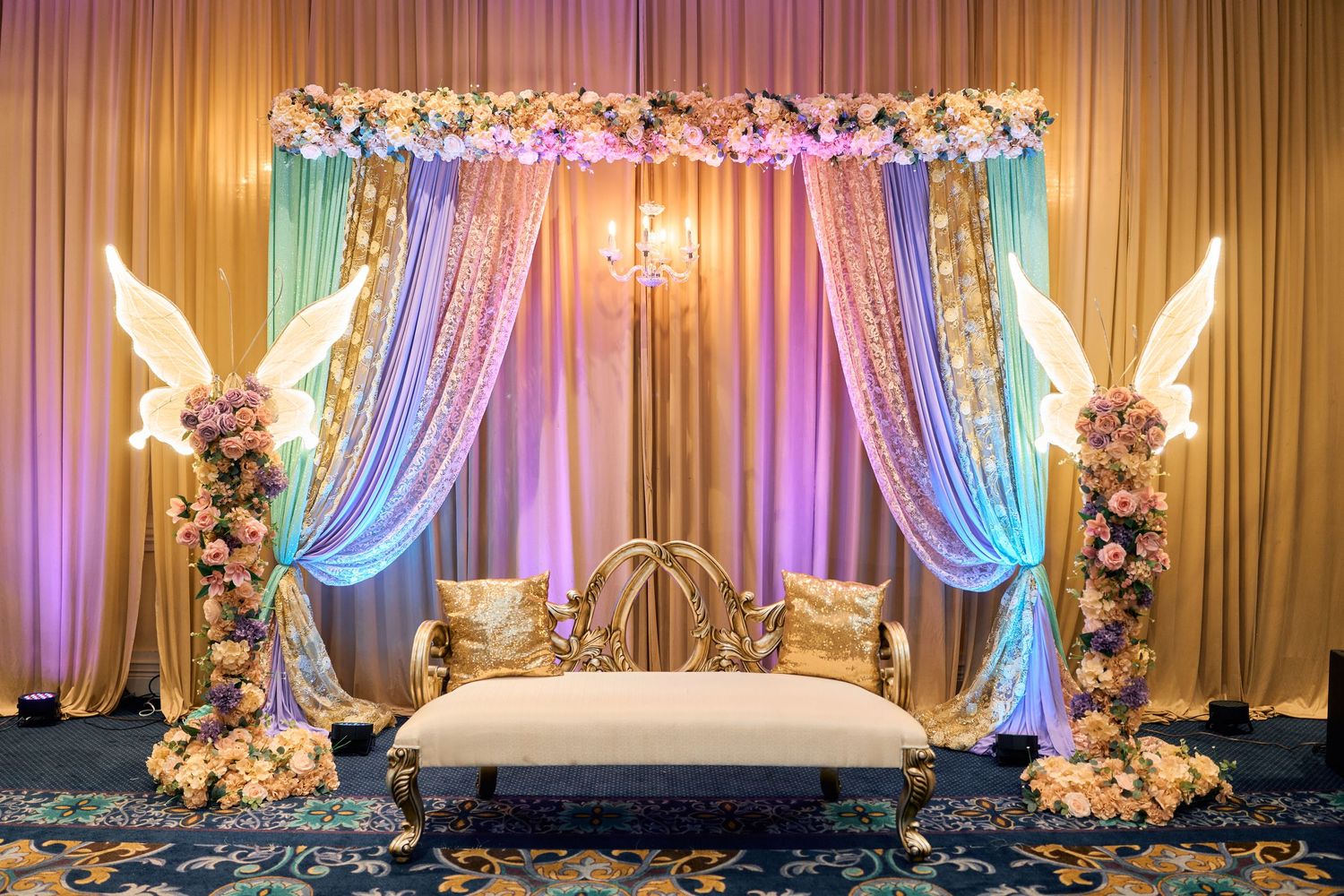 Luxury wedding stage with pastel drapes, floral arrangements, and elegant seating against a softly lit backdrop with gold accents.