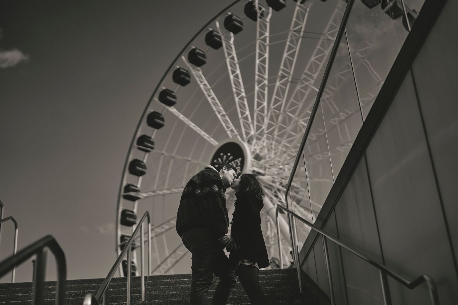 Silhouetted couple against a Ferris wheel at dusk in black and white.