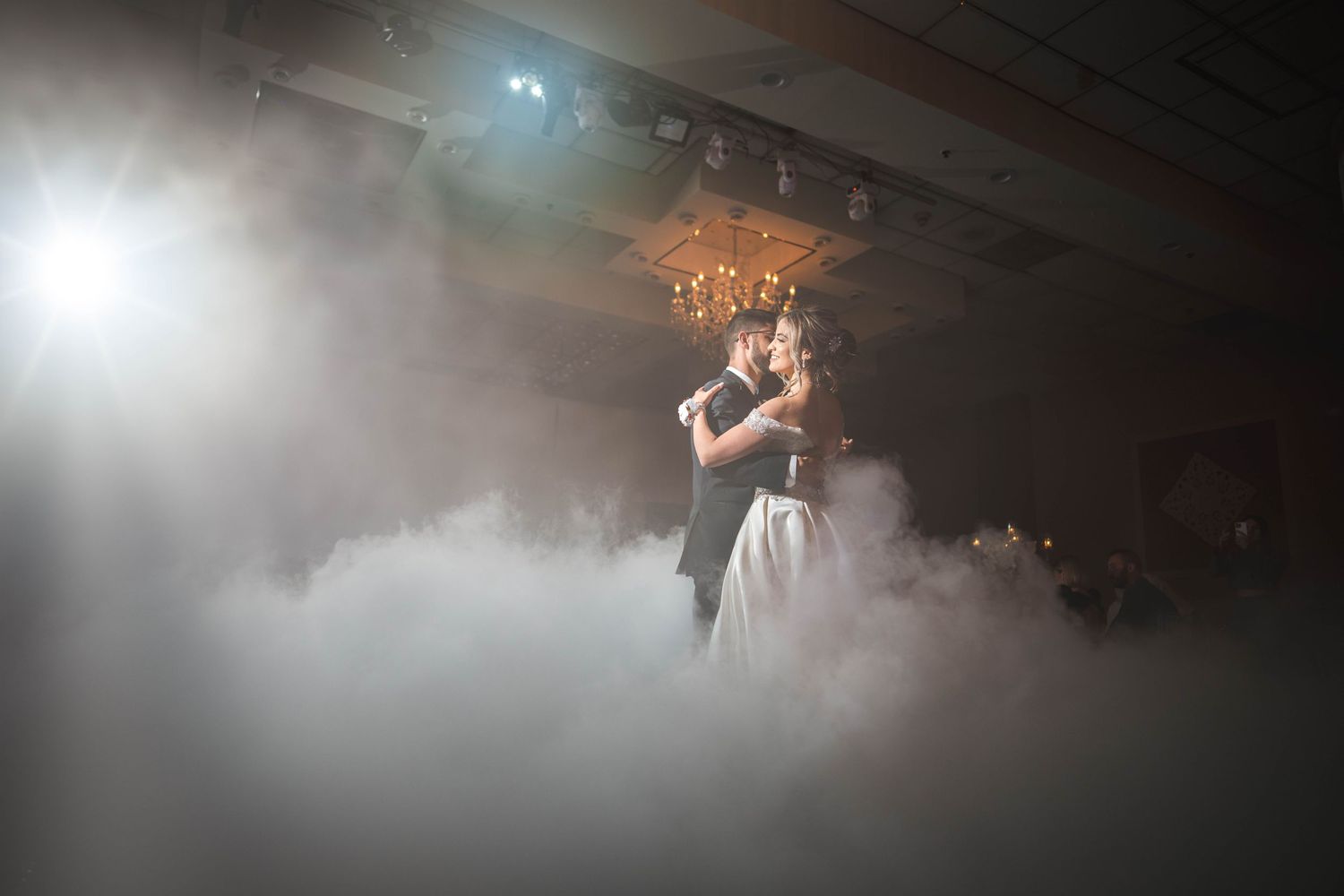 A couple's first dance at their wedding reception surrounded by dramatic fog and lighting effects on the dance floor.
