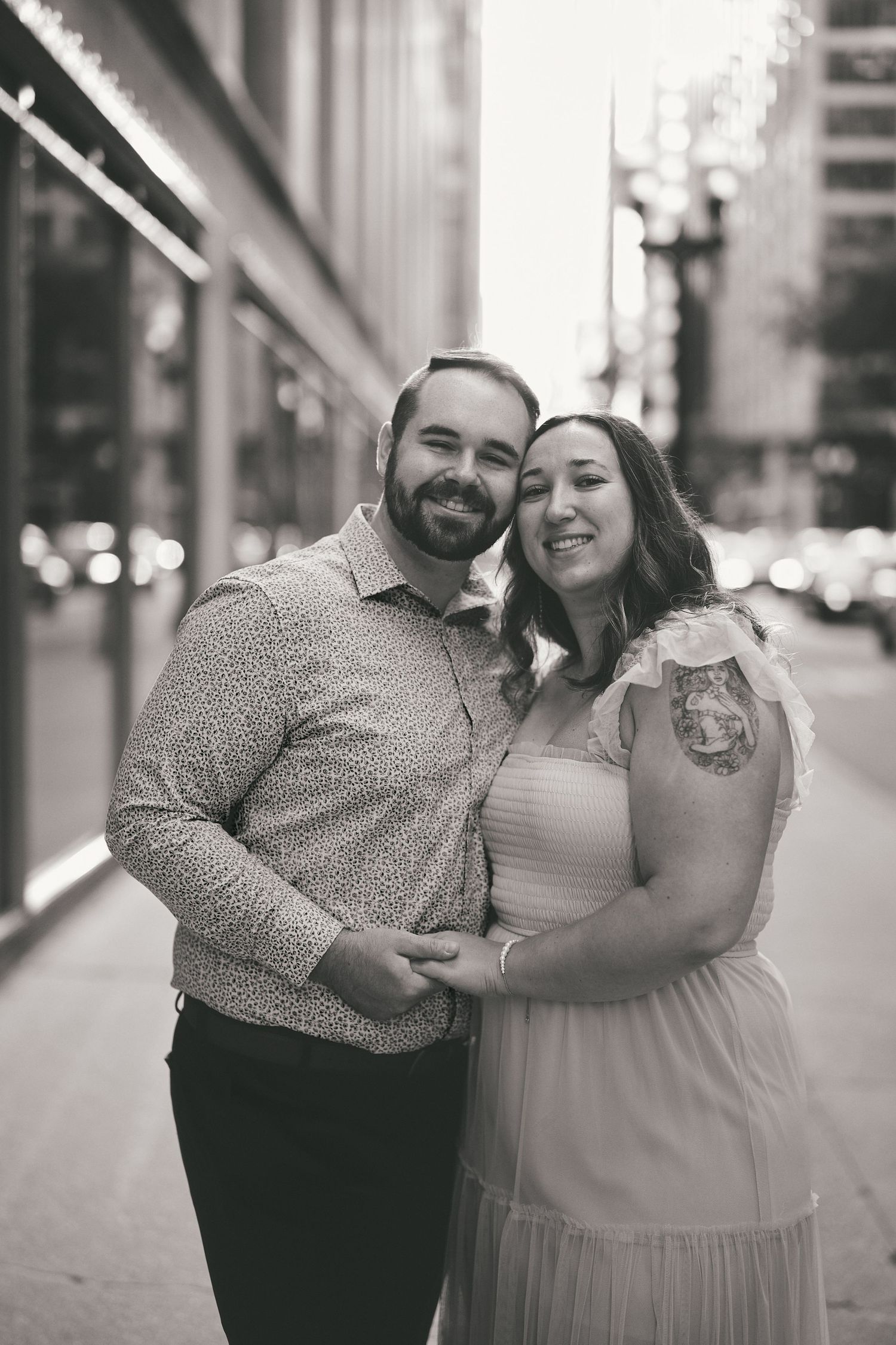 A happy couple embraces on a city street at dusk, wearing formal attire as they pose together.