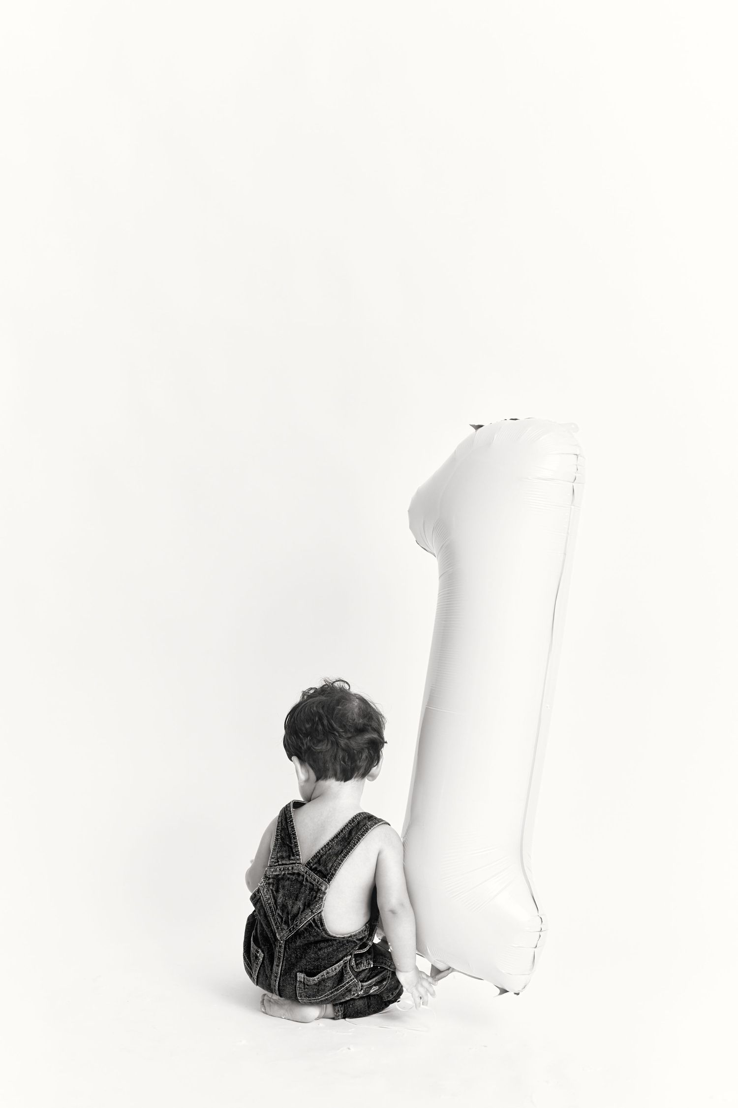 A minimalist black and white photo of a person sitting next to a tall white inflatable object against a plain backdrop.