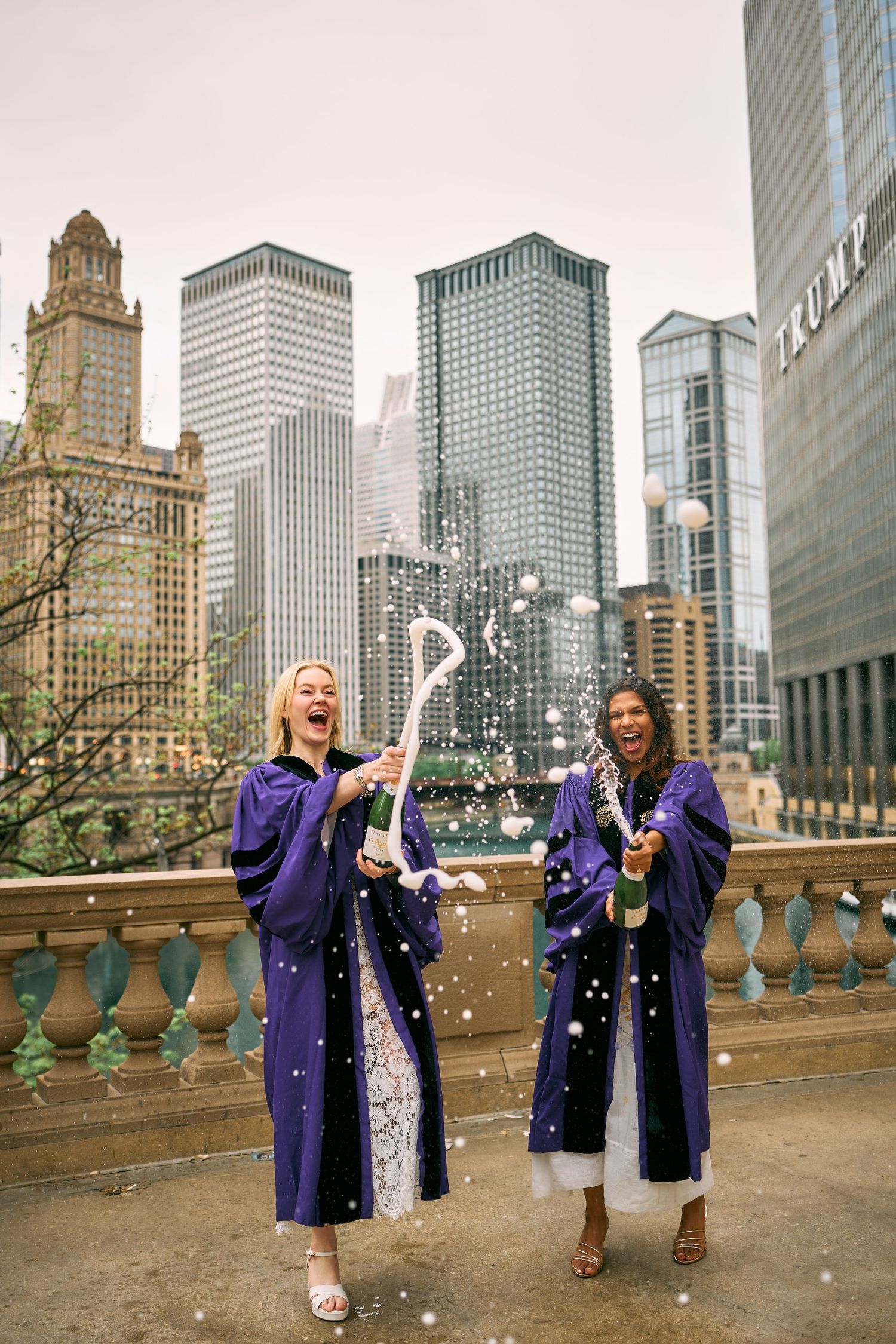 Two graduates in purple robes celebrate with confetti in downtown Chicago with skyscrapers in the background.
