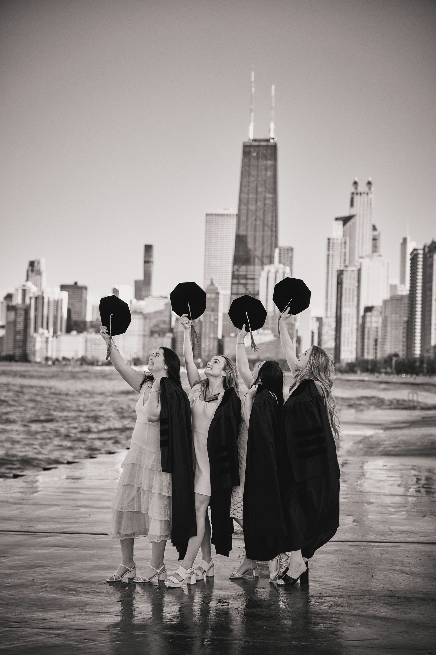 Four figures holding black balloons stand on a wet surface with Chicago's iconic John Hancock building skyline in background.