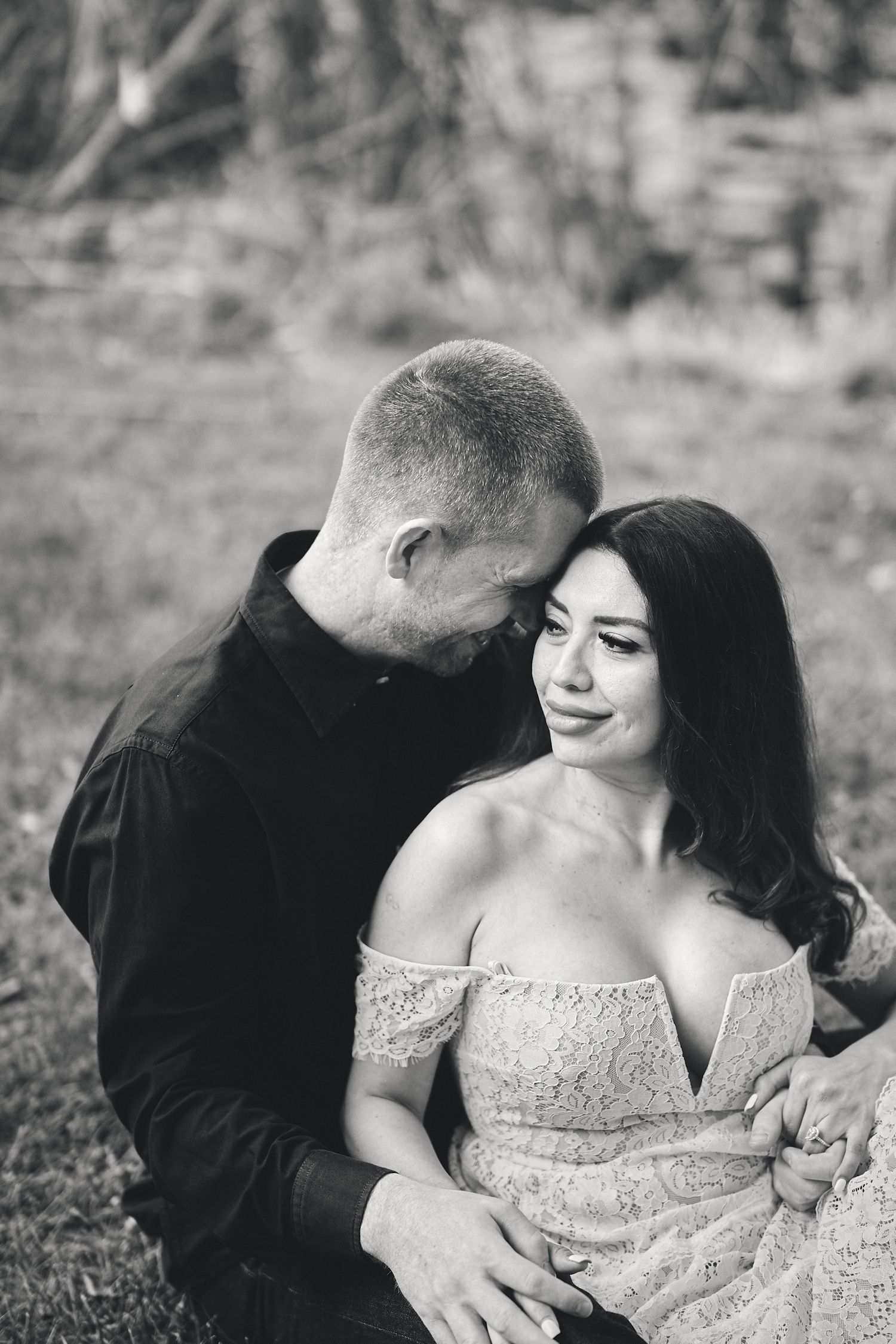 Black and white intimate portrait of a couple embracing outdoors, showing tender affection in soft natural lighting.