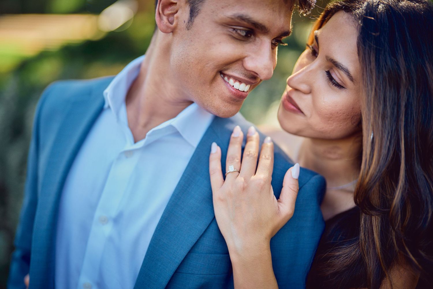 A couple shares an intimate moment outdoors with soft natural lighting while wearing a blue suit and casual attire.