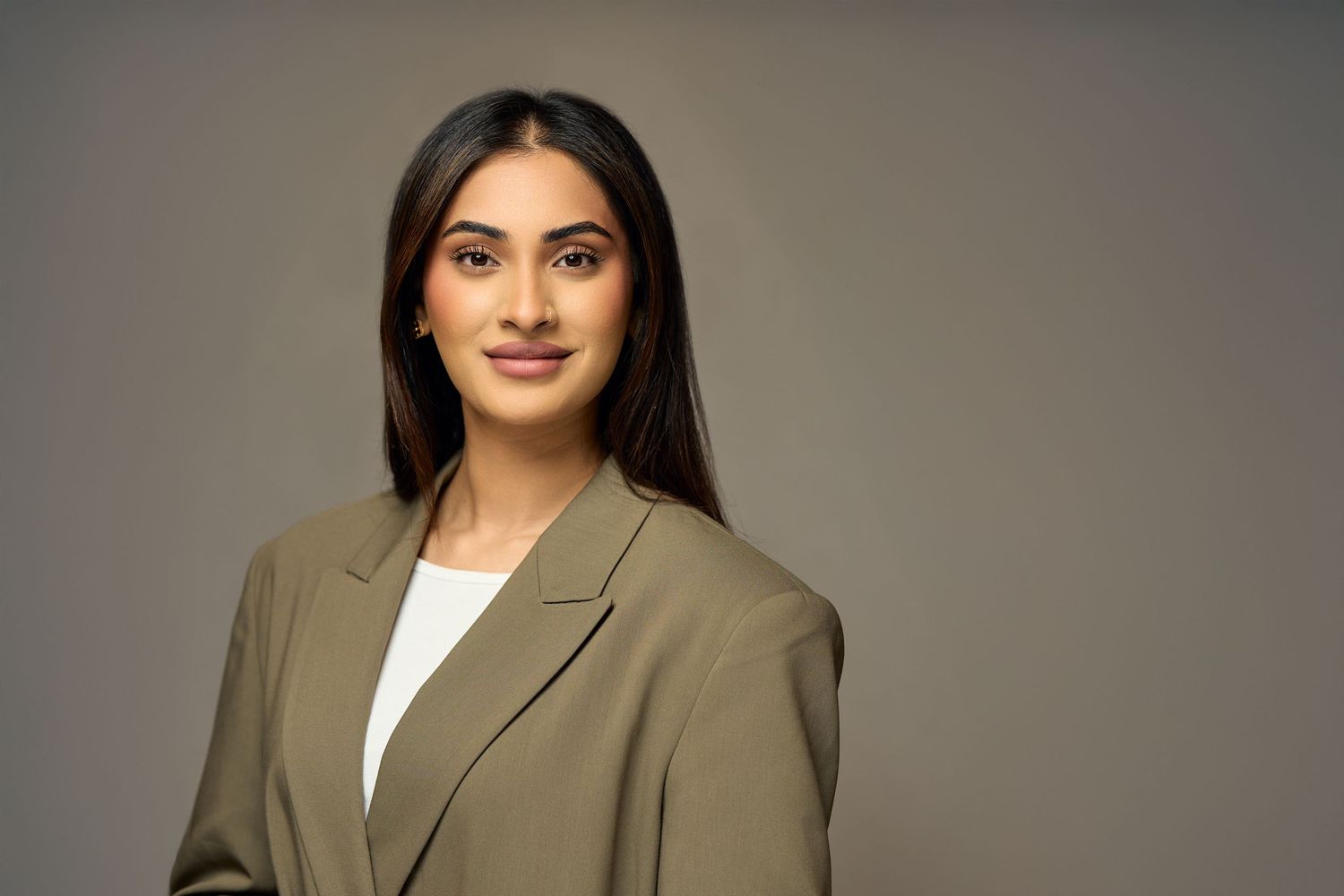 Professional headshot of person in tan blazer against dark background.