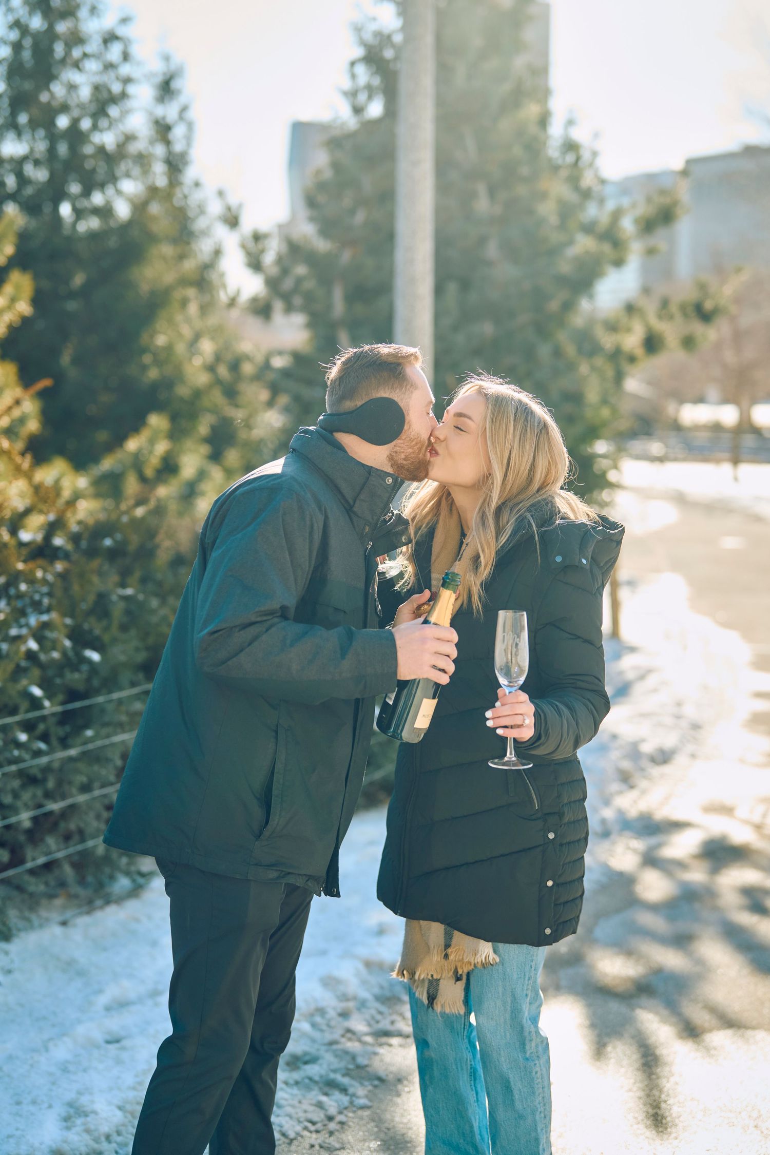 A winter scene as a couple shares an intimate moment while holding champagne glasses in the snowy outdoors.