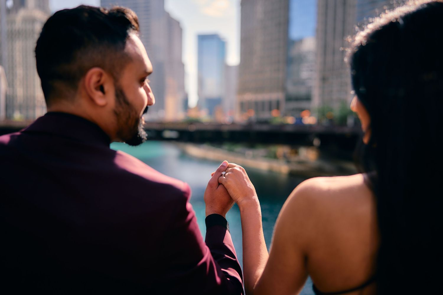 A couple holds hands while sitting along the Chicago River with the downtown skyline visible in the background.