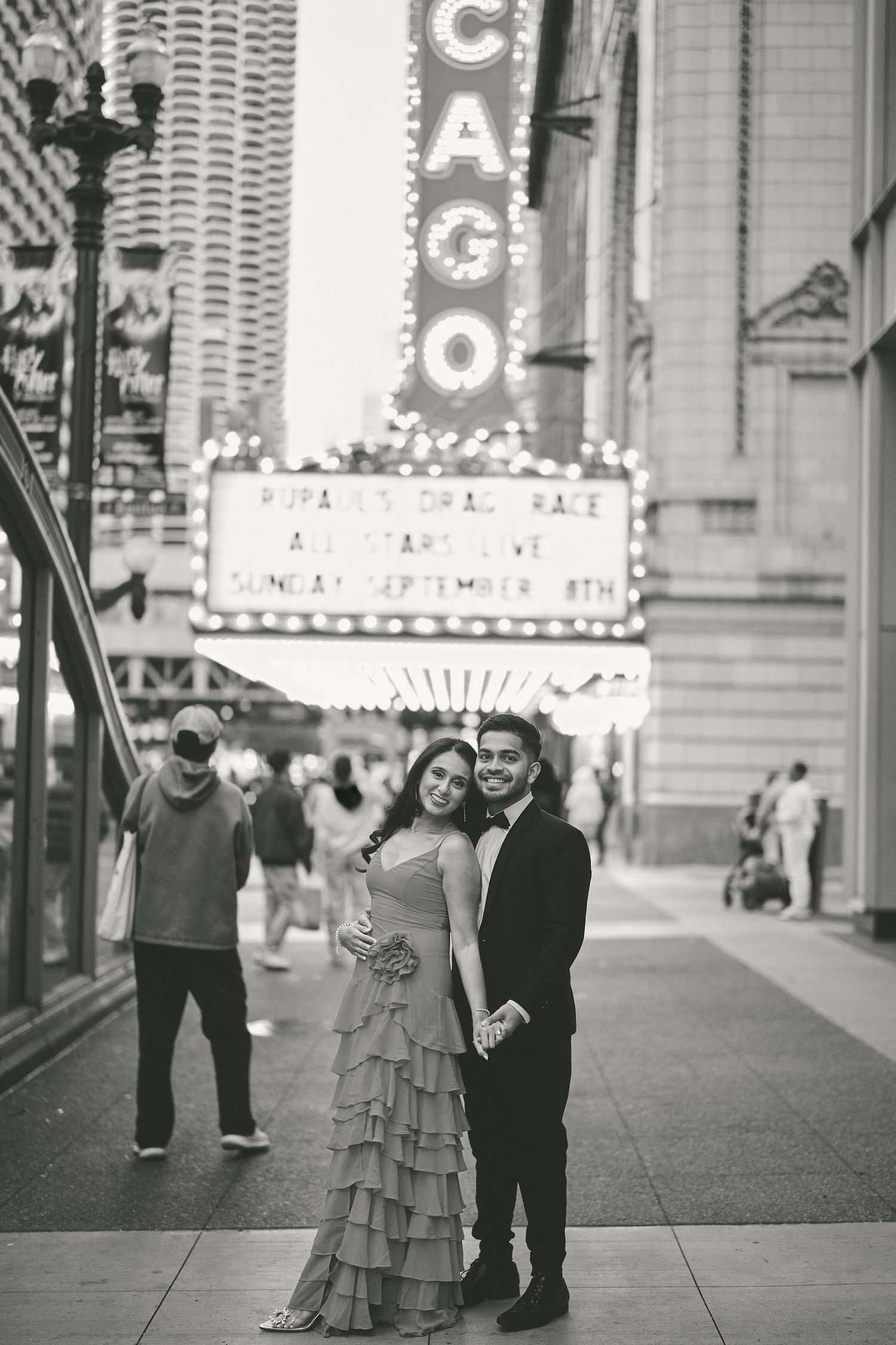 A black and white photo of a couple posing together in front of the iconic Chicago Theater marquee.