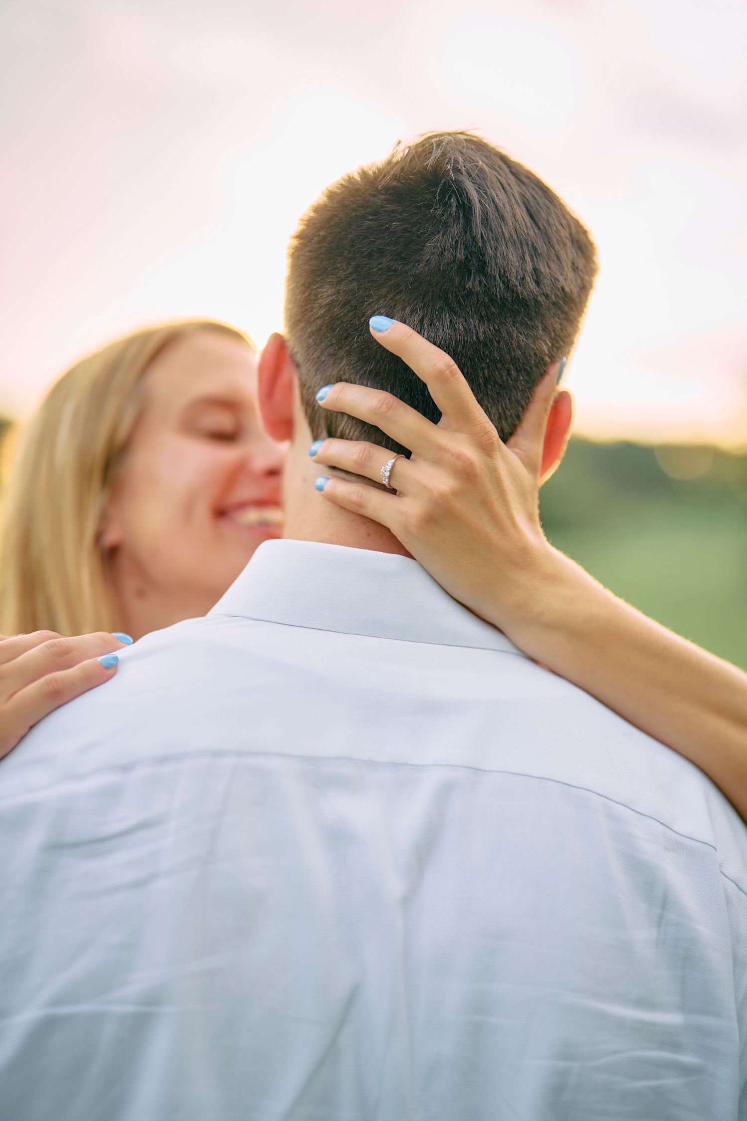 Close-up shot of a couple embracing outdoors at sunset with woman's hand gently touching her partner's neck.