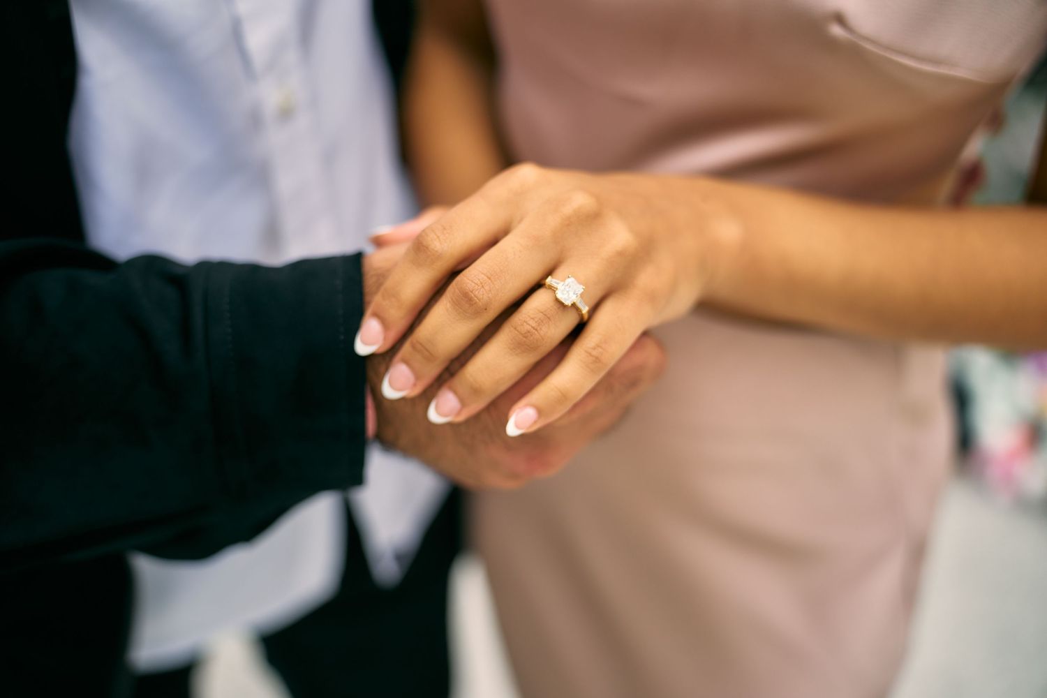 Close up shot of two hands with one wearing an engagement ring in soft lighting.