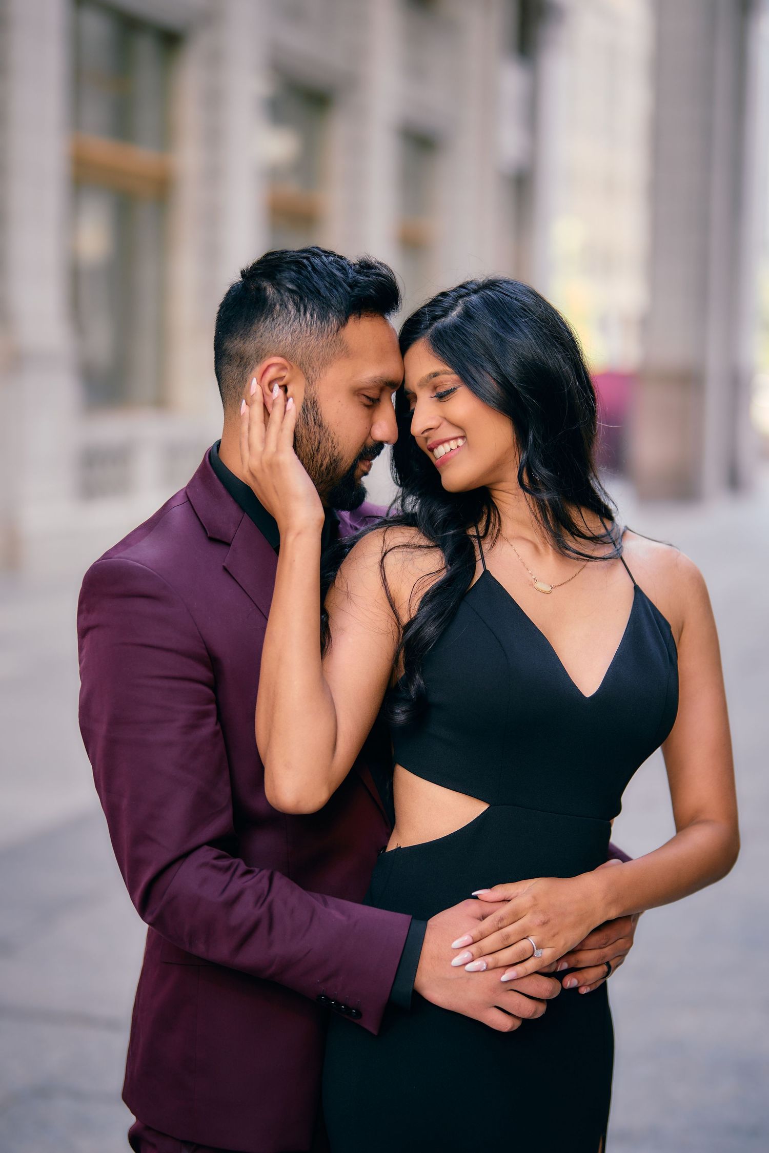 Romantic couple sharing an intimate moment in formal attire, with him in burgundy suit and her in black dress.