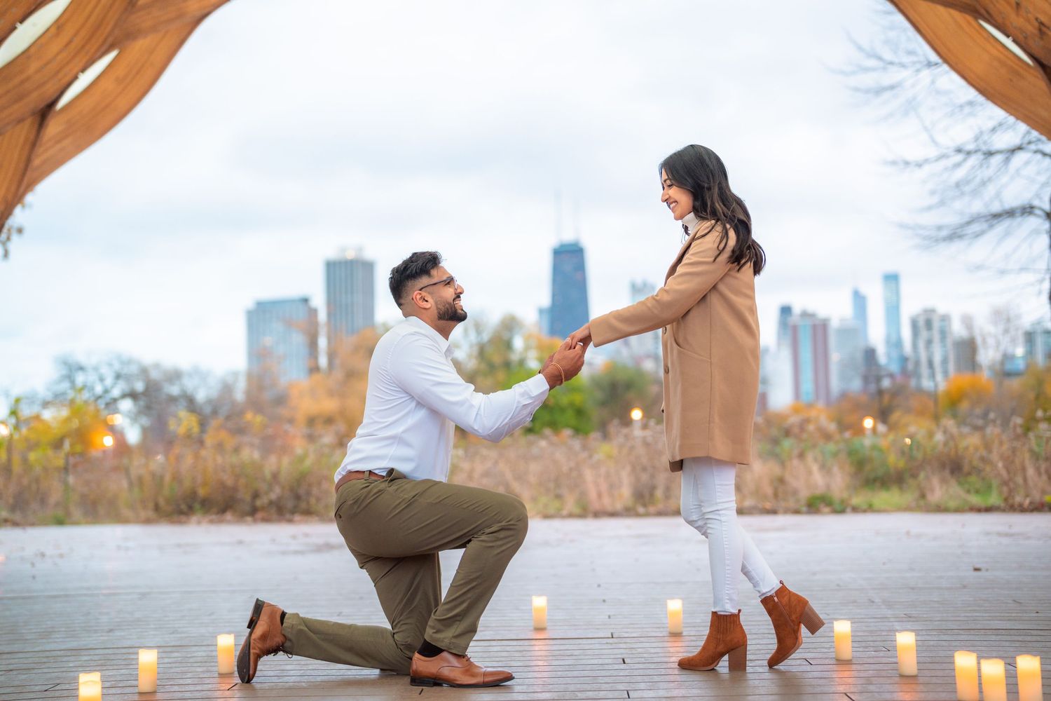 A romantic proposal scene with candles on a deck overlooking a cityscape during autumn.
