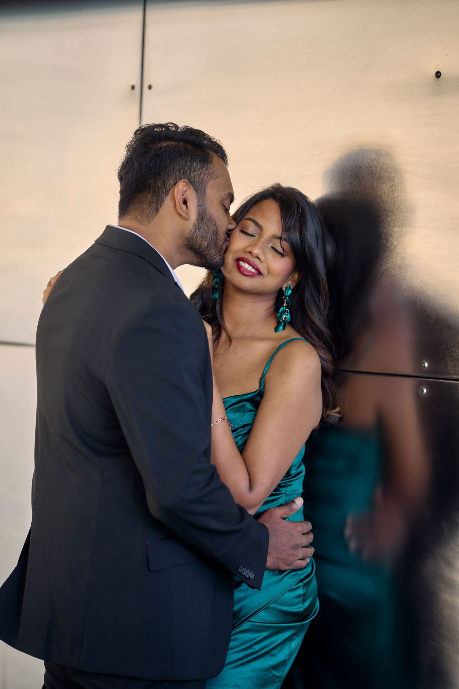 A romantic moment between two people, with one in a black suit and the other in a stunning teal evening dress.