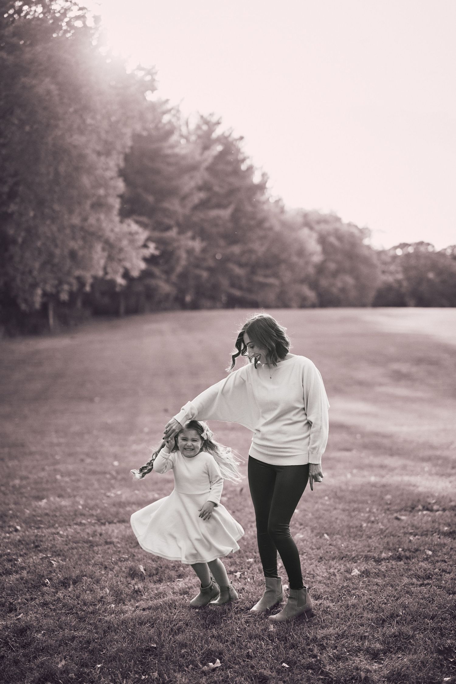 A joyful moment captured in black and white as two people dance and twirl together in a grassy field beside trees.