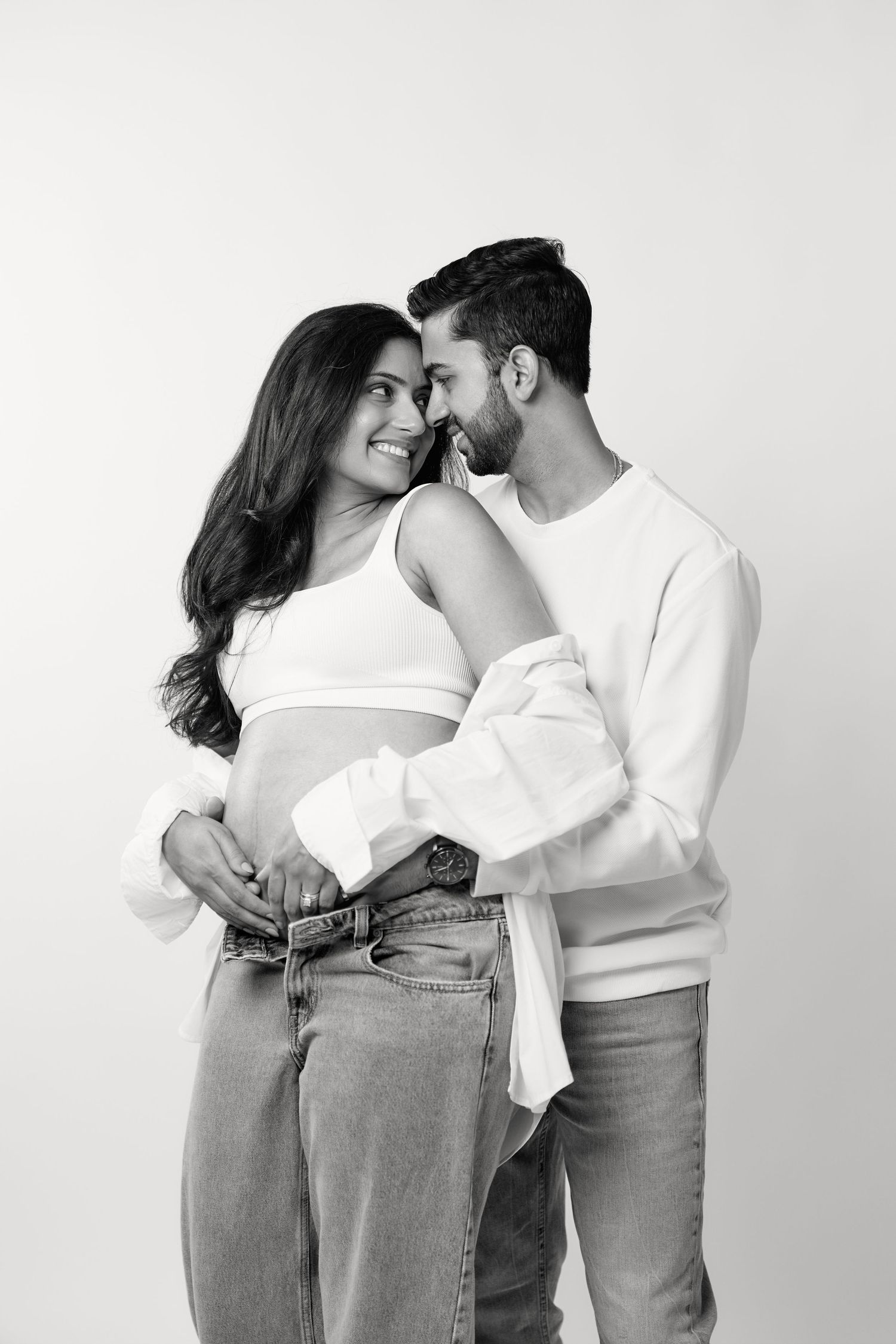 A romantic couple in white tops and jeans embraces intimately against a white background in a series of tender poses.