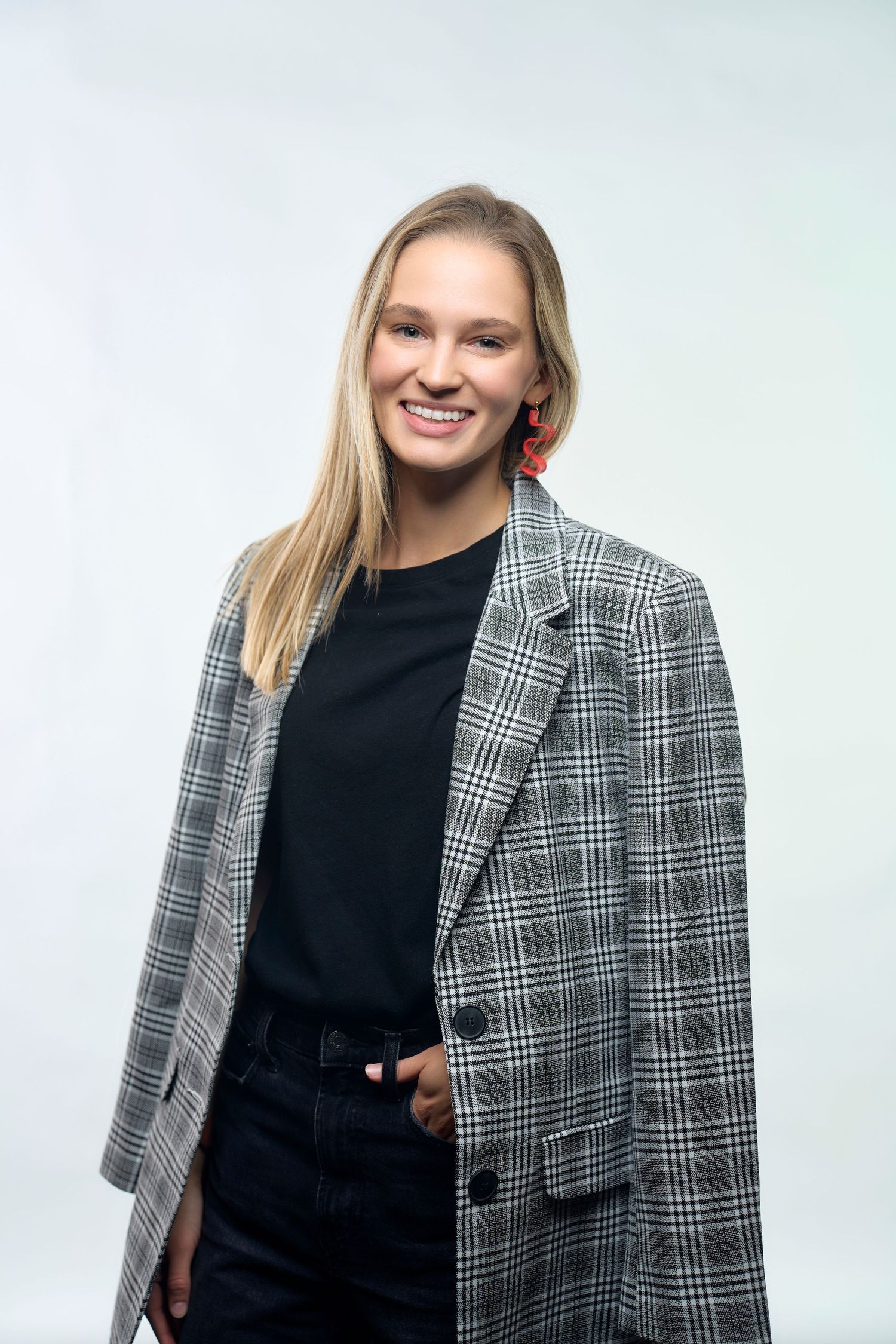 Professional portrait of person wearing plaid blazer over black outfit against white background.