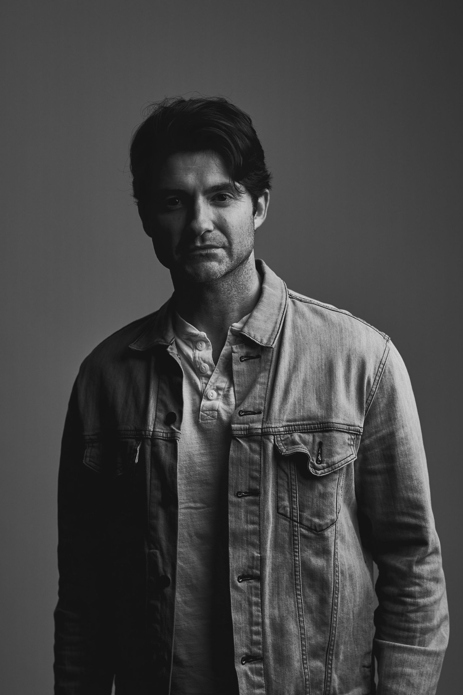 Moody black and white portrait of man wearing light denim jacket.
