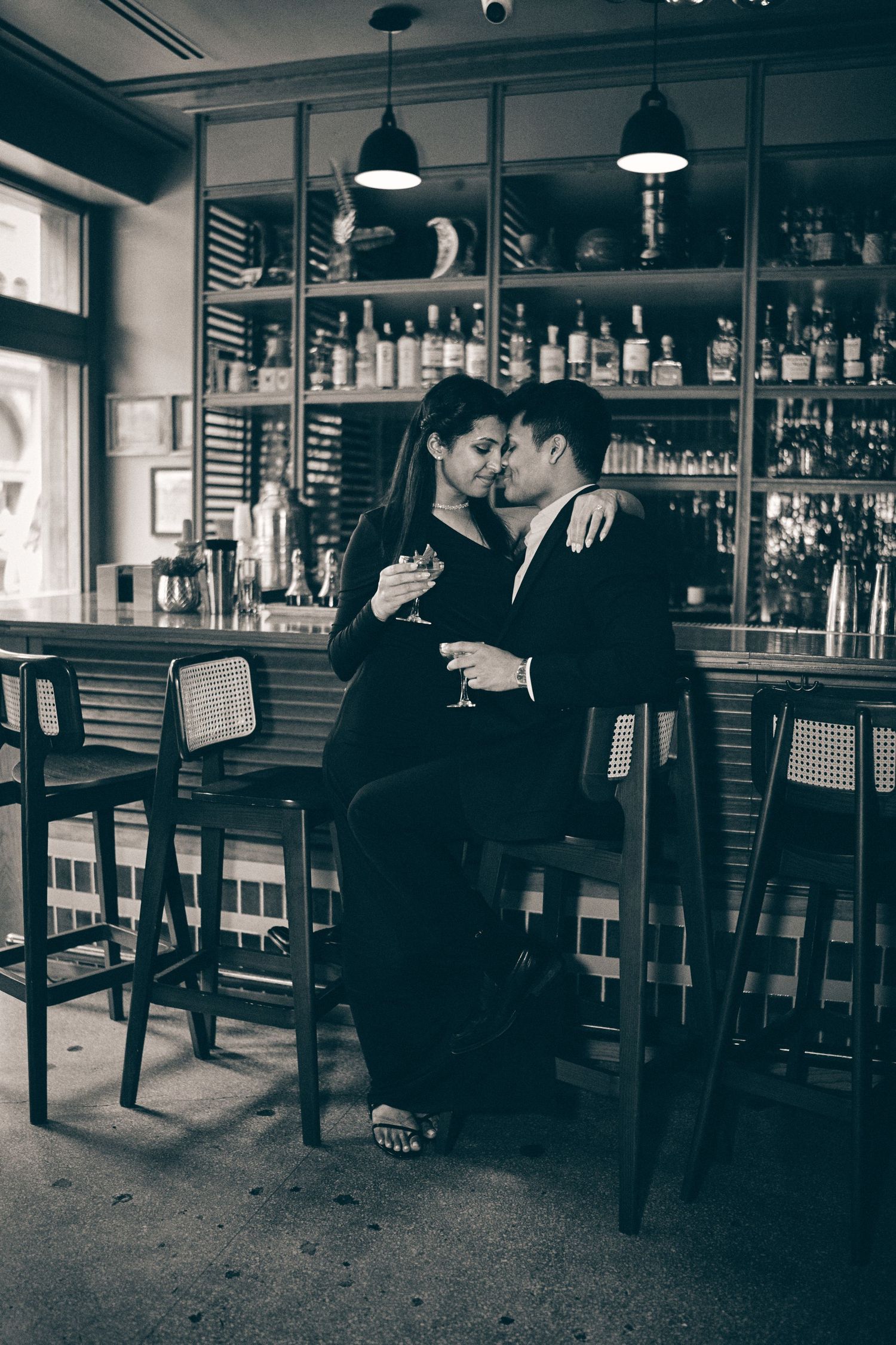 A romantic couple embraces at a bar counter, sharing an intimate moment in black and white vintage style photography.
