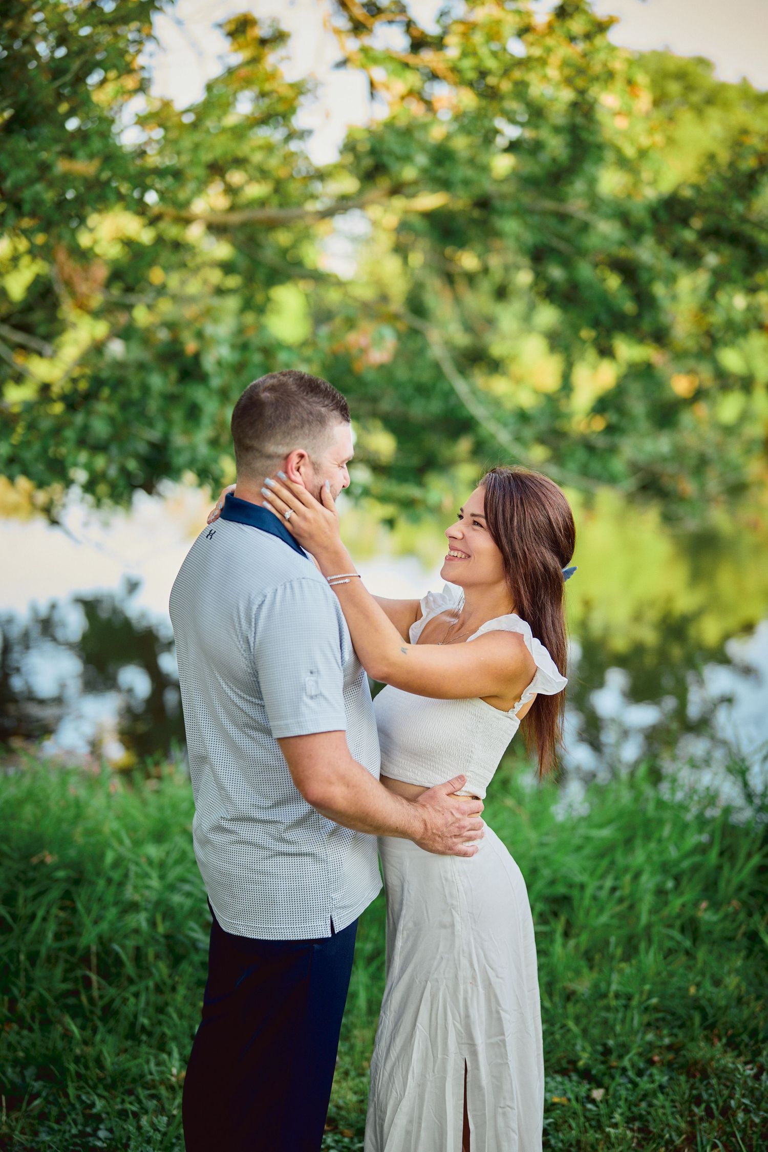 A romantic couple embraces outdoors in a natural setting with lush greenery and soft lighting.