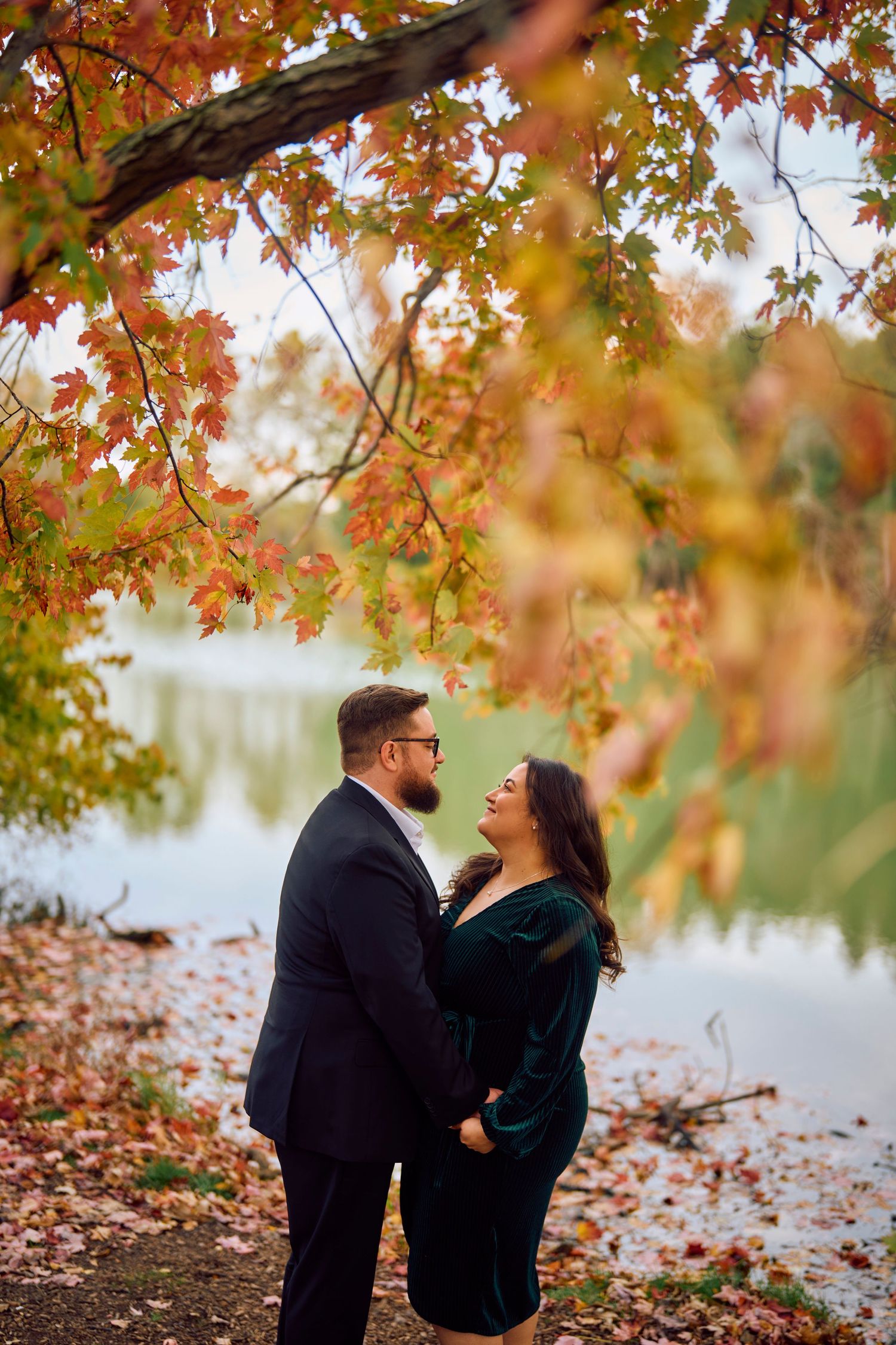 A couple shares a romantic autumn moment beneath colorful maple trees by a serene lake.