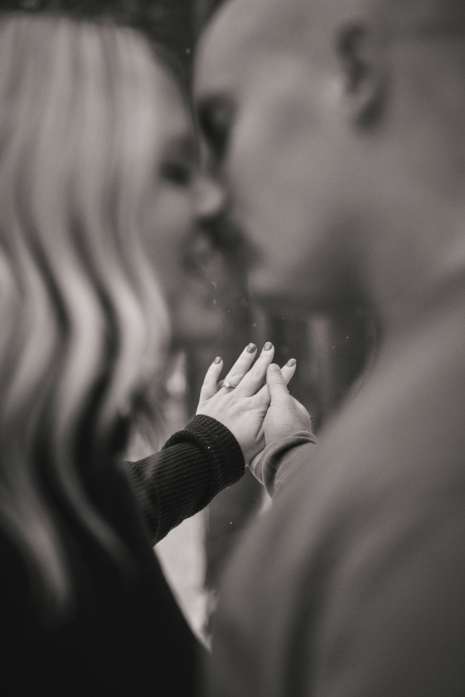 A romantic close-up black and white photo showing two people holding hands while about to kiss.