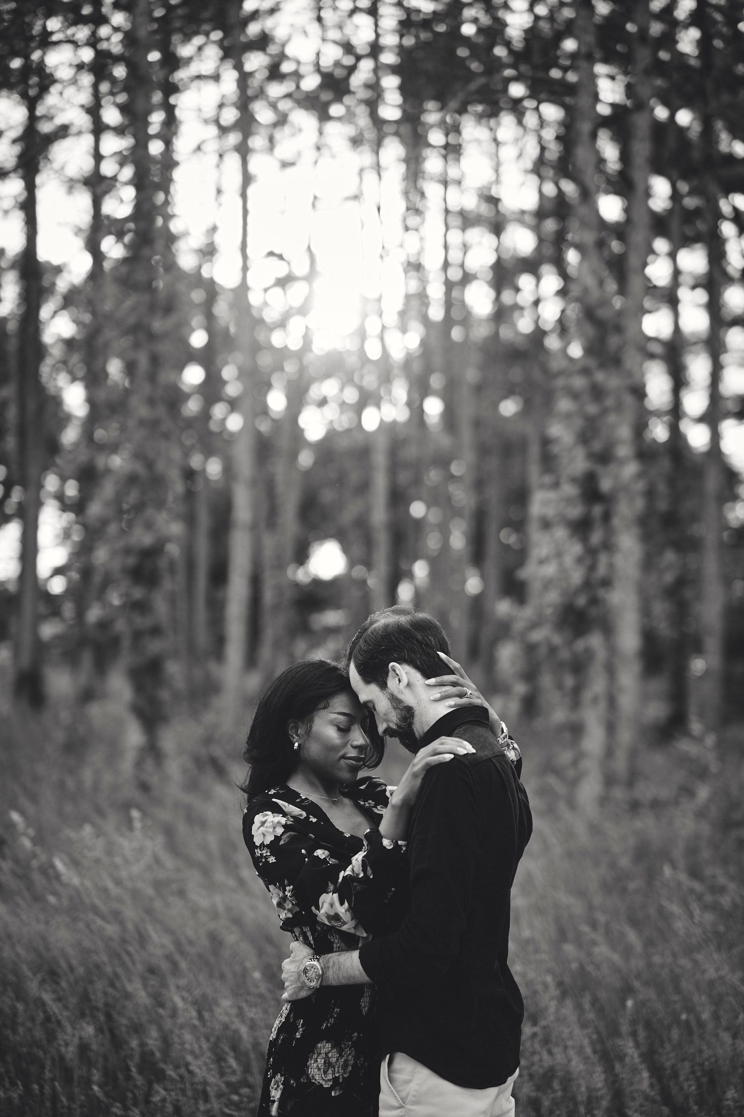 A tender black and white romantic moment between two people embracing in a sunlit forest.